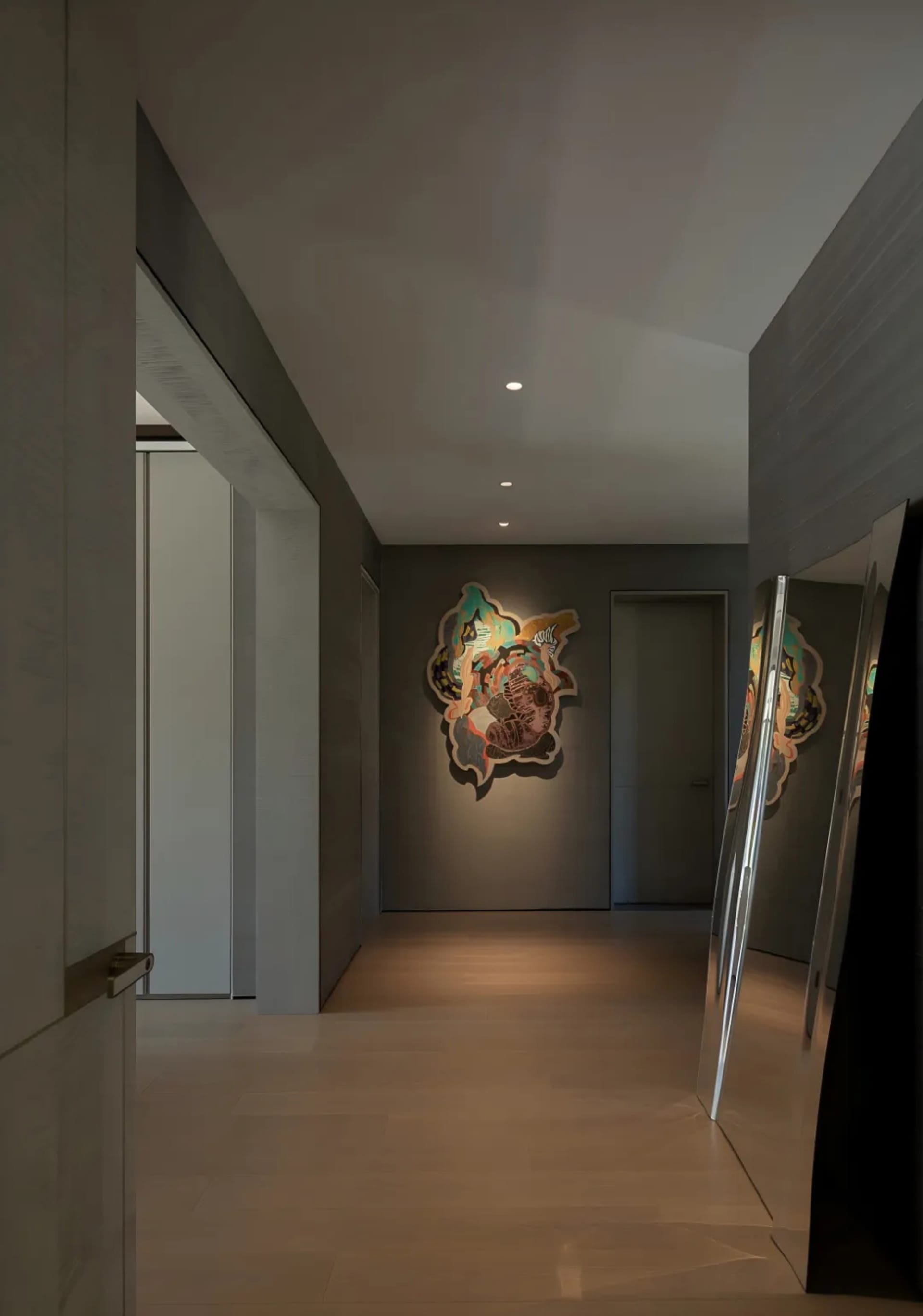 A modern hallway with a large mirror, a painting, and wooden surfaces, featuring two doors and clean lines