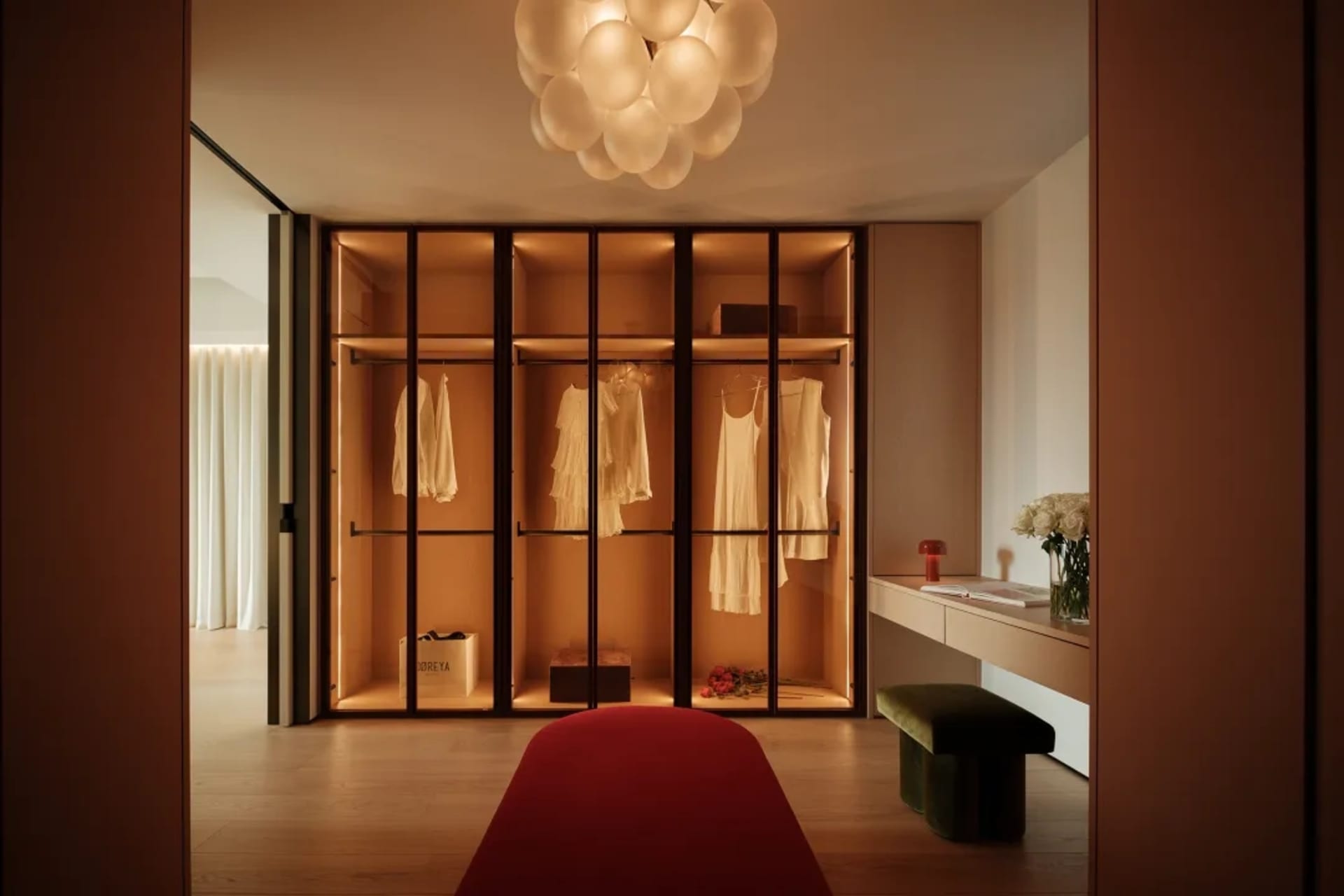 A well-lit bedroom with wooden floors, a red carpet, two wooden closets, a bed, and decorative vases
