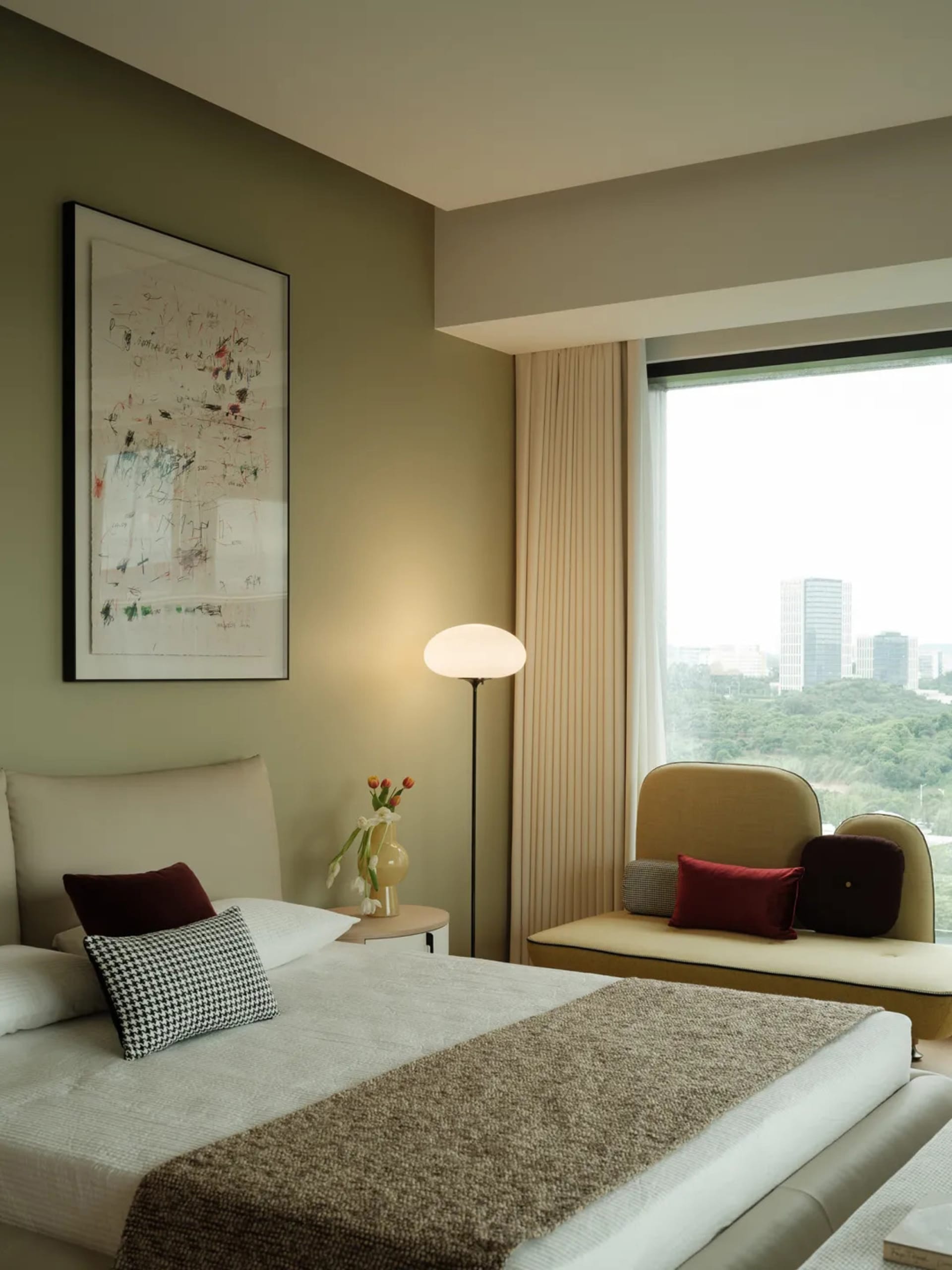 Well-lit bedroom with a large window, two couches, a chair, and a bed, featuring white walls and wooden elements