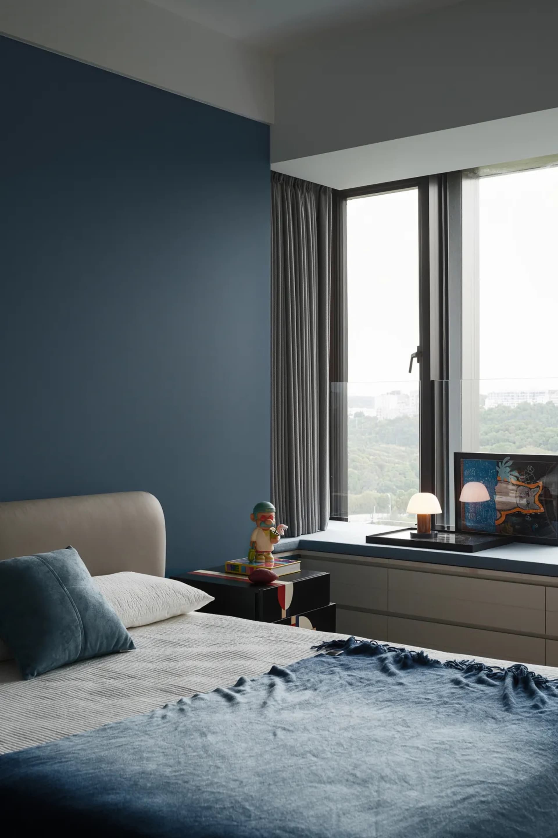 Cozy bedroom with two beds, a chair, and books, featuring a large window with natural light and a white color scheme