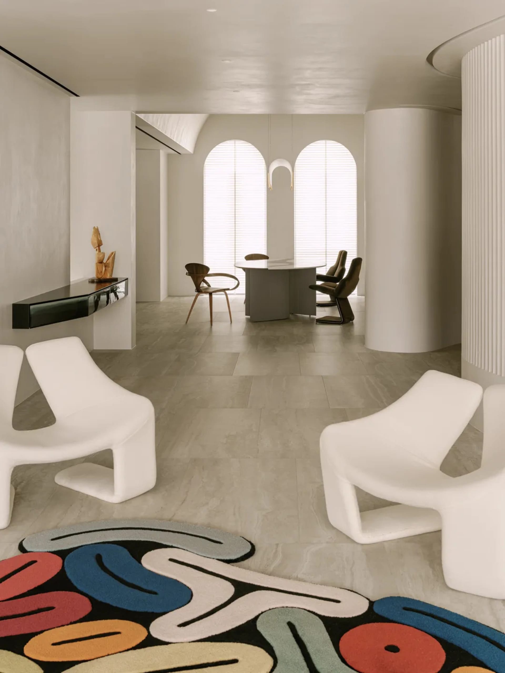 Open modern living space with white chairs and tables, natural light from a large window, and a minimalist design