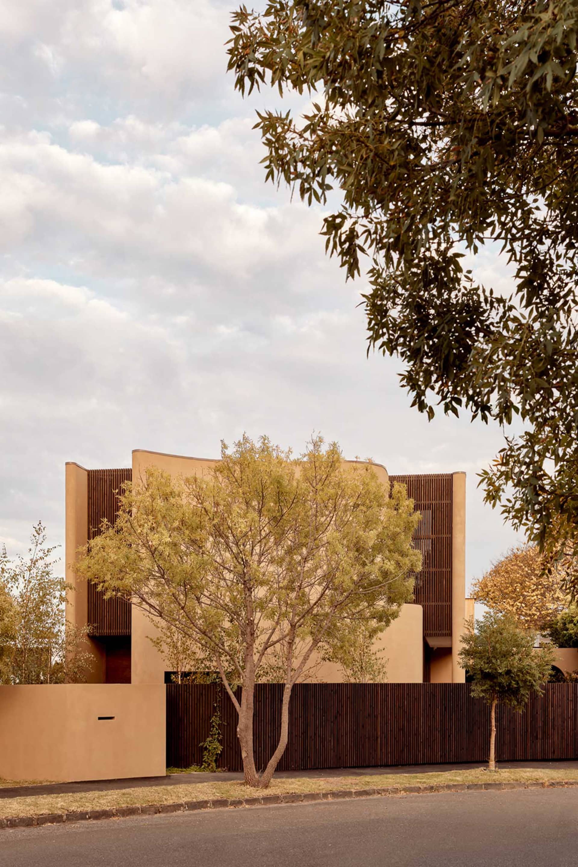 A tan house with a green tree and bushes in the foreground, set against a natural background