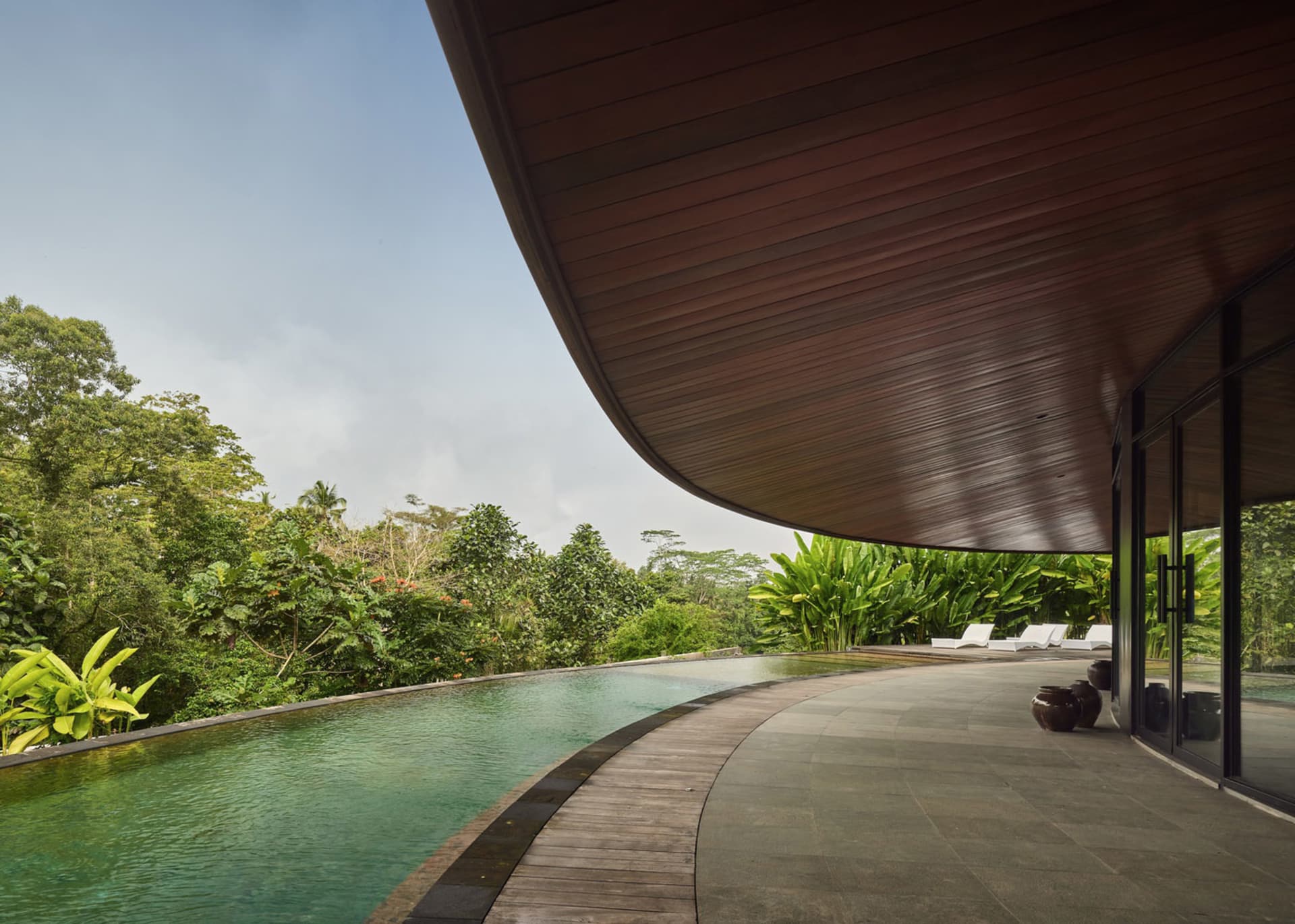 A large building with a wooden exterior and a swimming pool in front, surrounded by chairs for relaxation and socializing