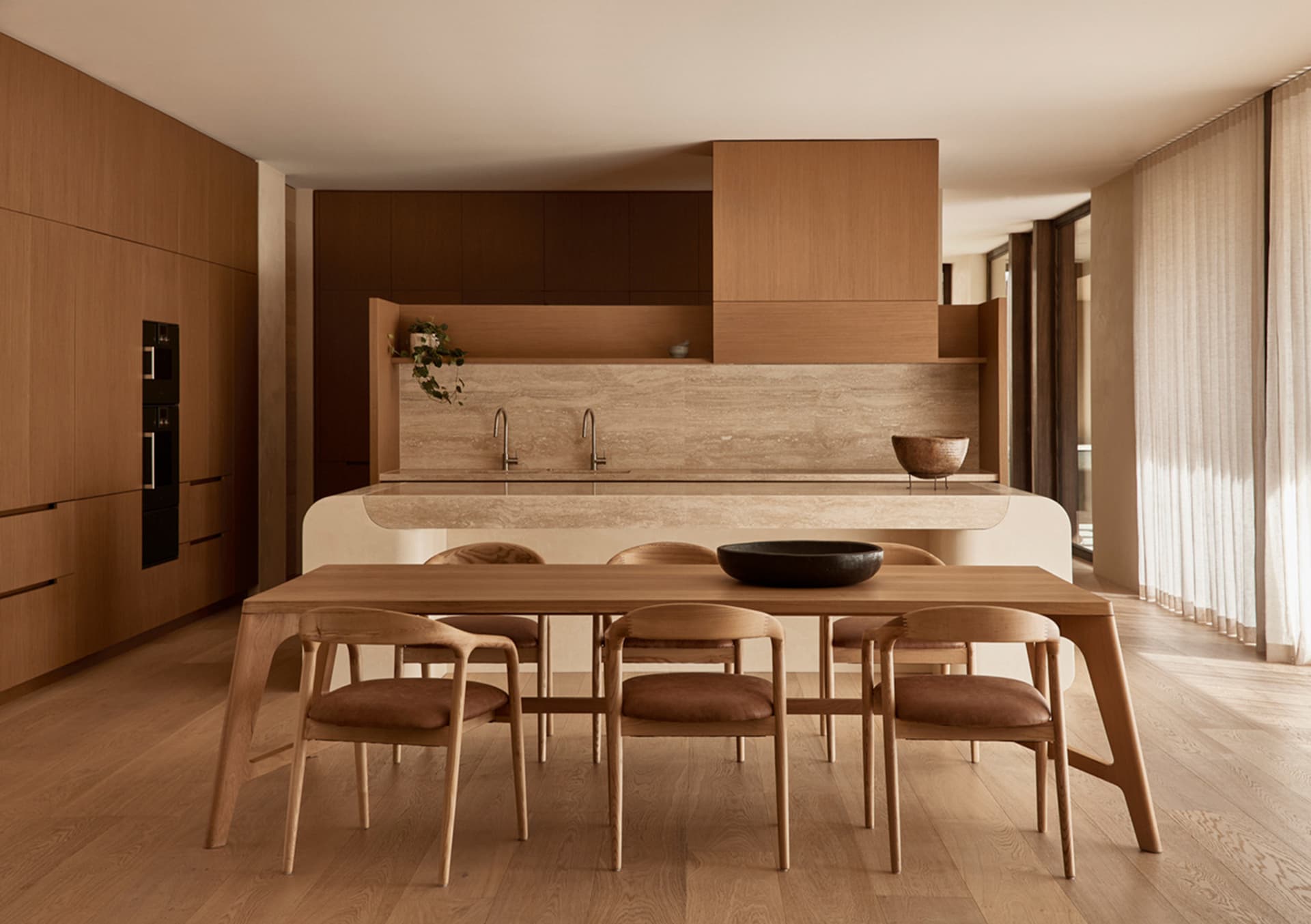 A modern kitchen with wooden floors and cabinets, featuring two dining tables and chairs, creating a clean and inviting atmosphere
