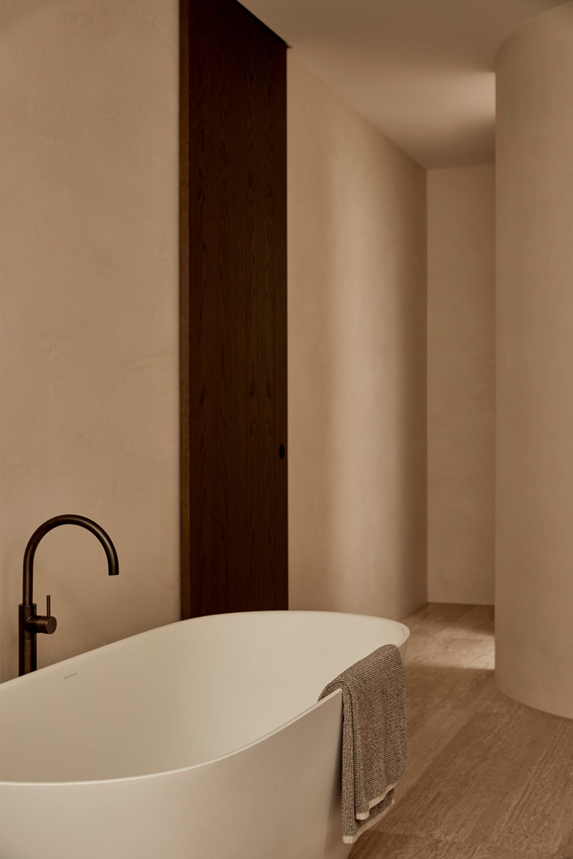 A serene bathroom with a white bathtub in front of a brown door, minimalist design, and no visible people