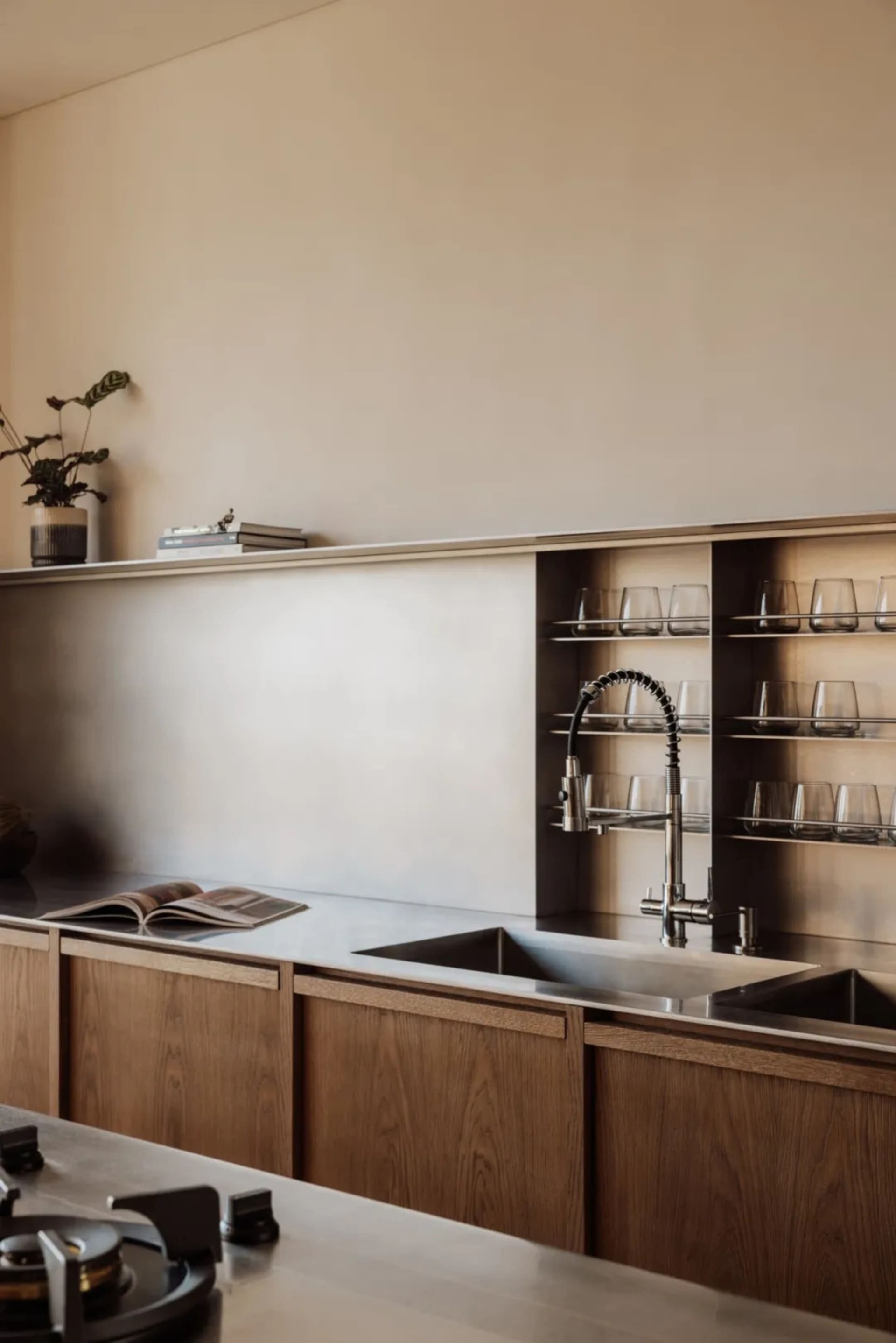 A modern kitchen with stainless steel countertops, a sink, cabinets, and a bookshelf, featuring wine glasses and books