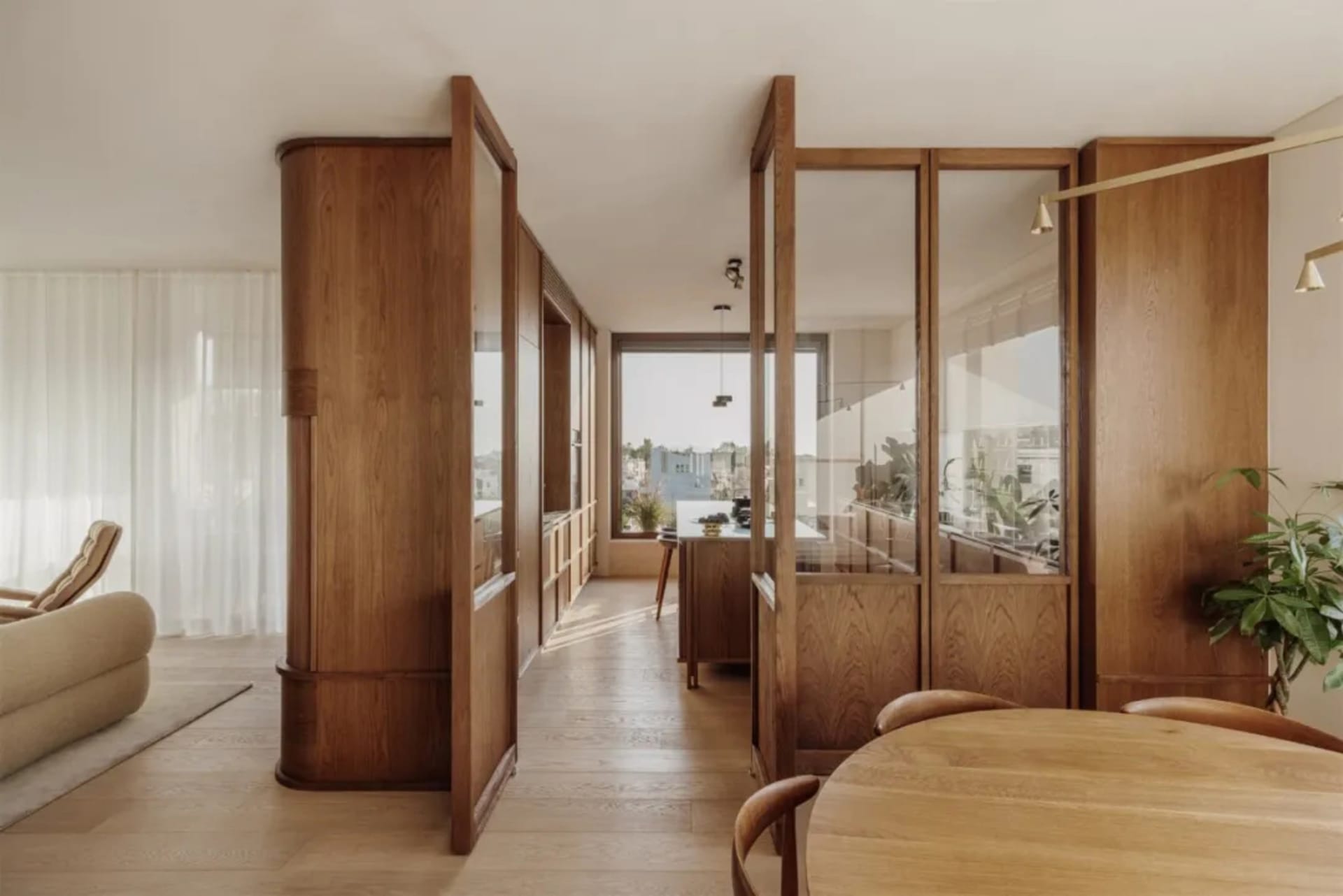 Warm and inviting open concept living area with wooden floors and walls, natural light from large windows, a dining table, and potted plants
