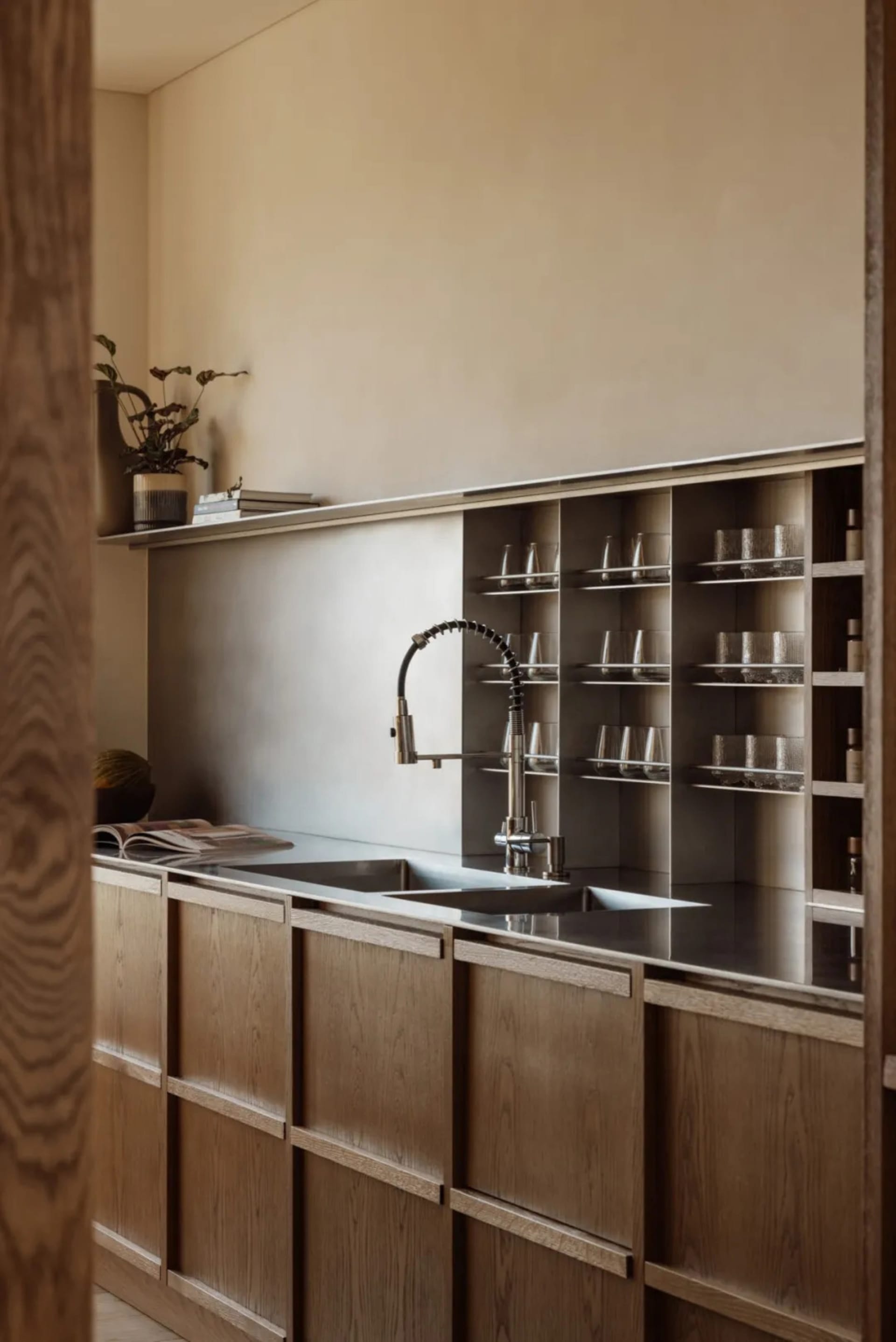 A cluttered kitchen with a sink, cabinets, and various items on the countertops, including wine glasses and scattered books