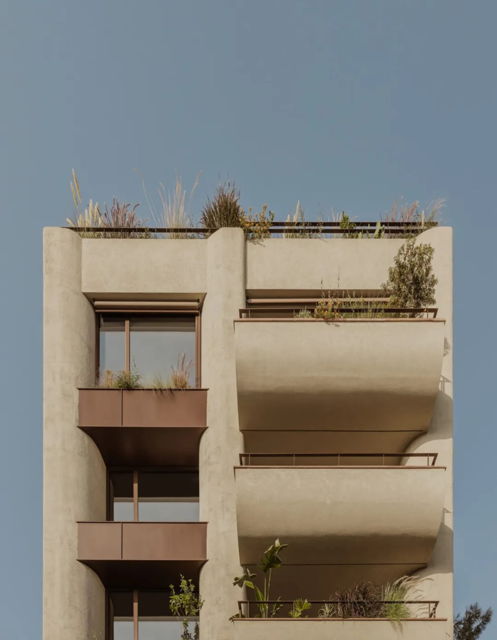 Exterior view of a modern high-rise building with gray and brown tones, featuring windows, potted plants, and a sophisticated design