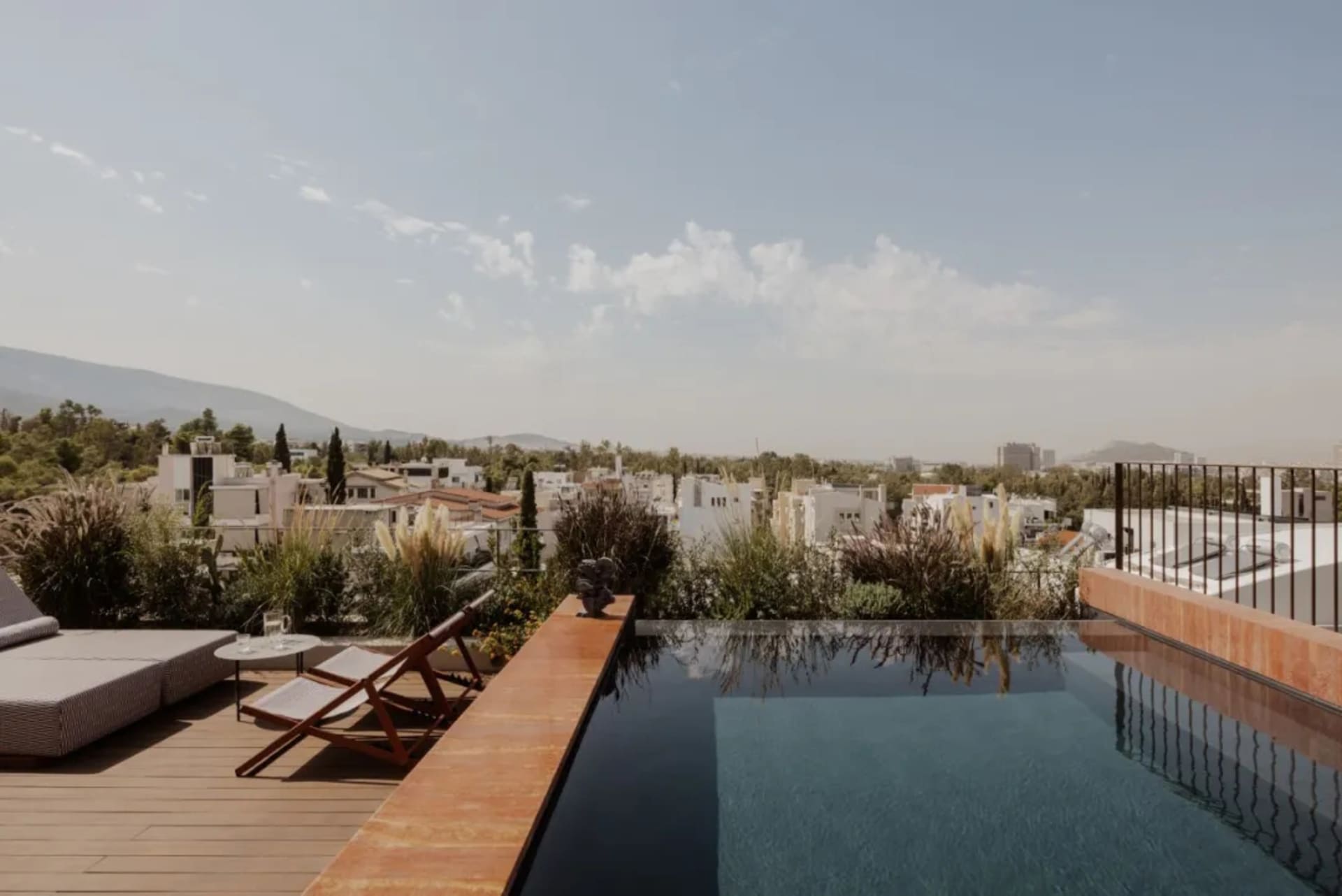 A rooftop pool area with two chairs, surrounded by trees and city buildings, creating a relaxing atmosphere