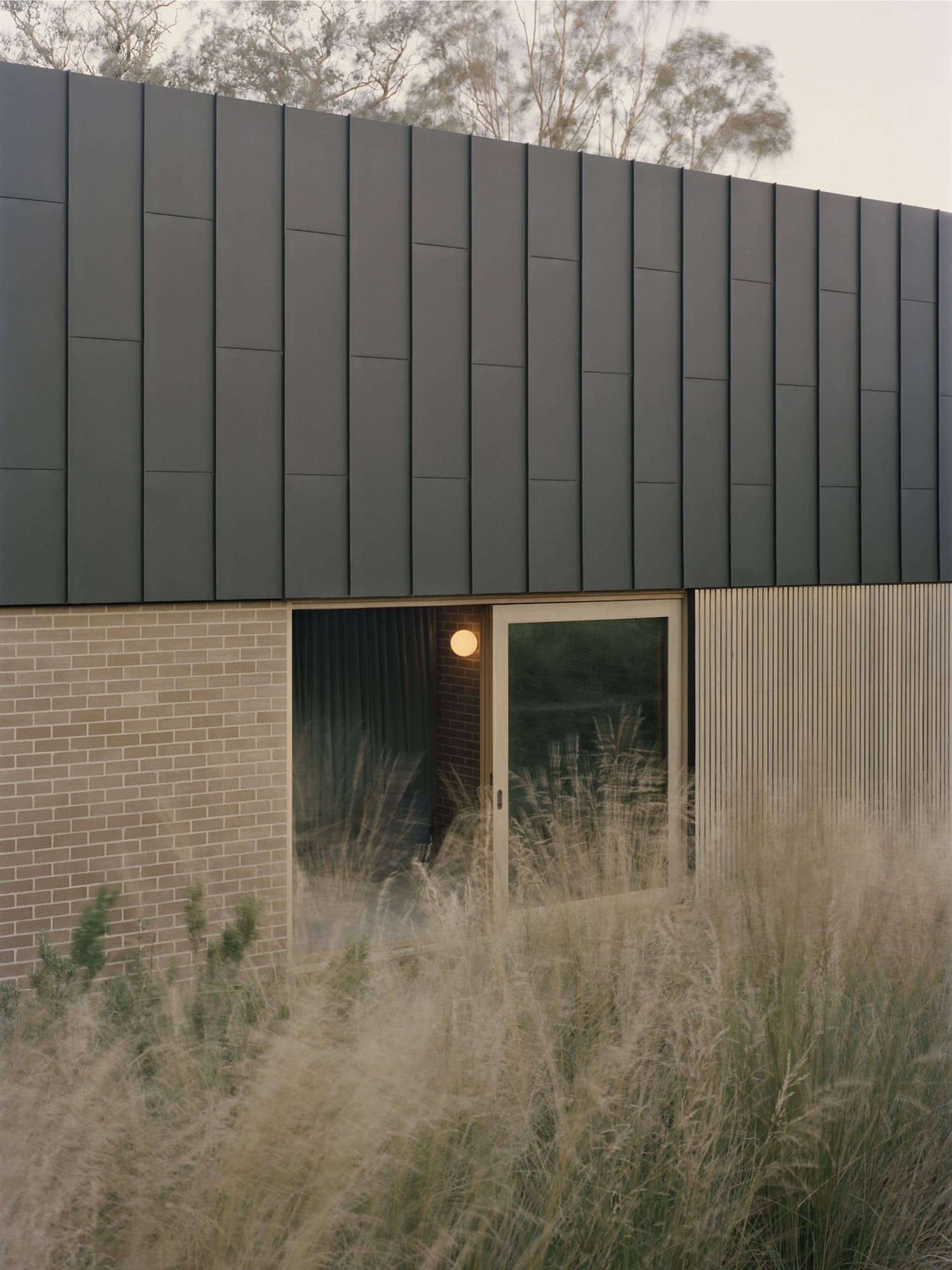Exterior view of a house with a black roof, brick wall, and natural light from windows