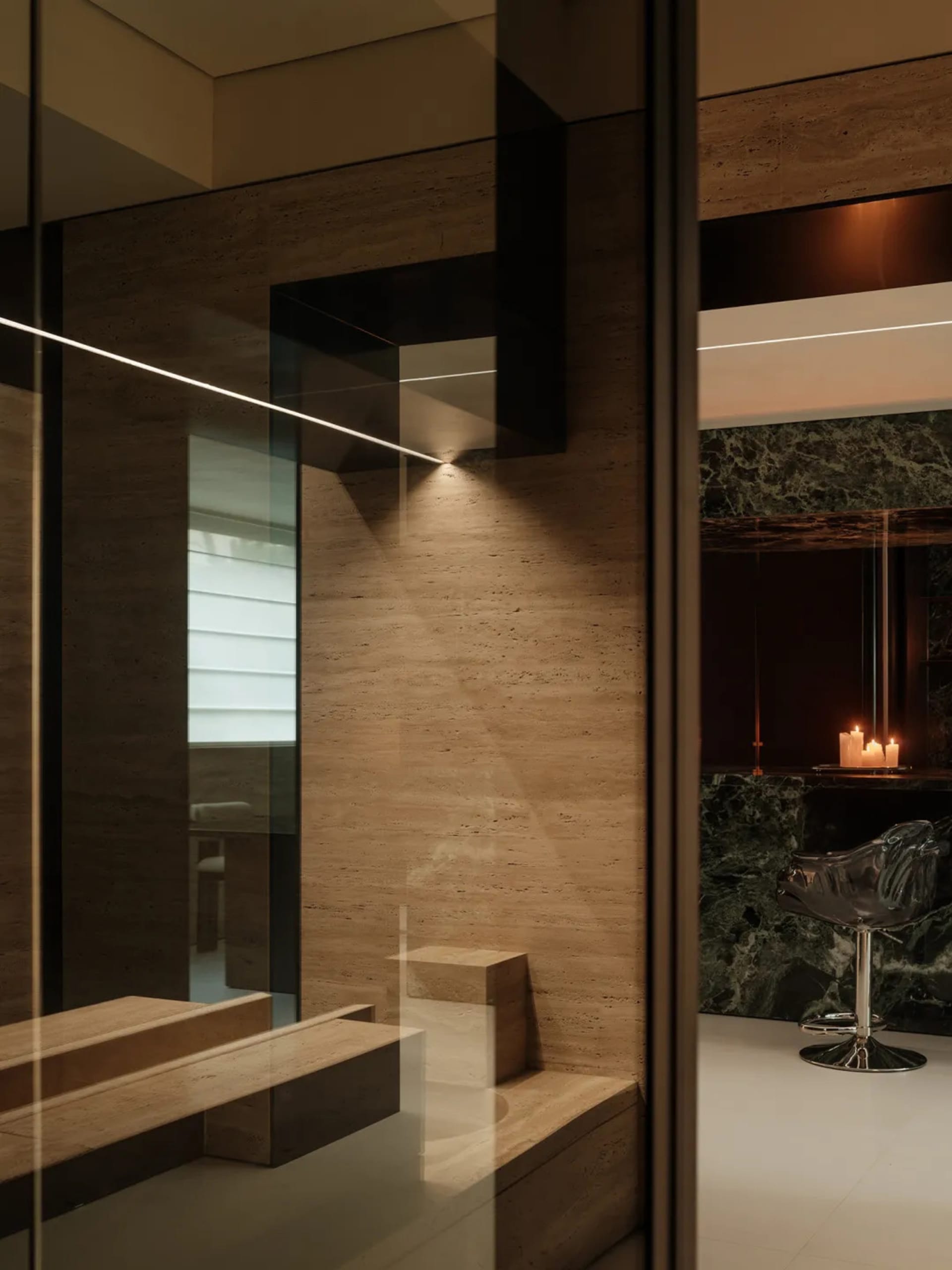 Modern bathroom with a large marble countertop, wooden bench, two chairs, and a candle, featuring a clean and minimalist design