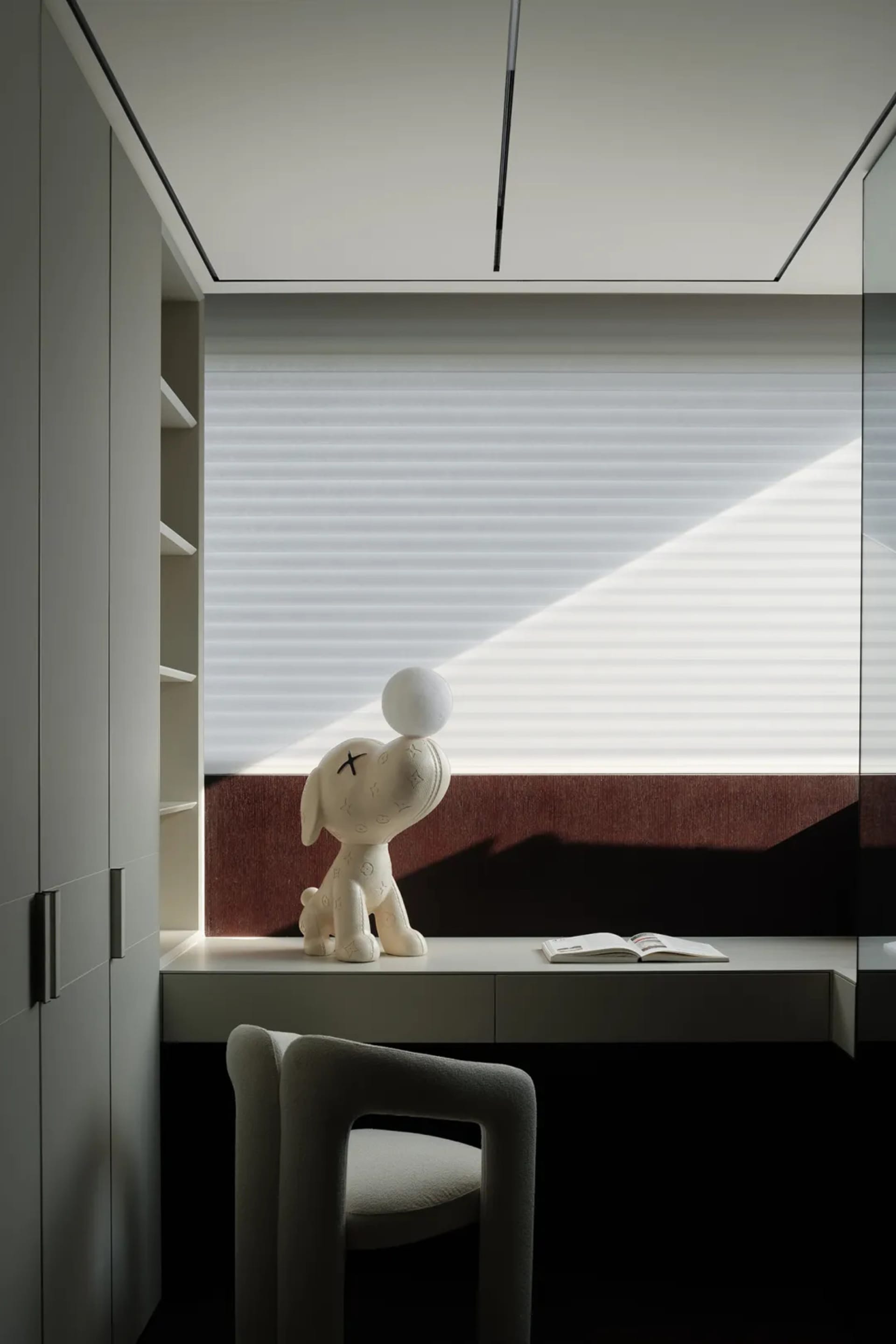A calm and inviting study with a white dog figurine on a wooden desk next to a window, a black chair, and books nearby
