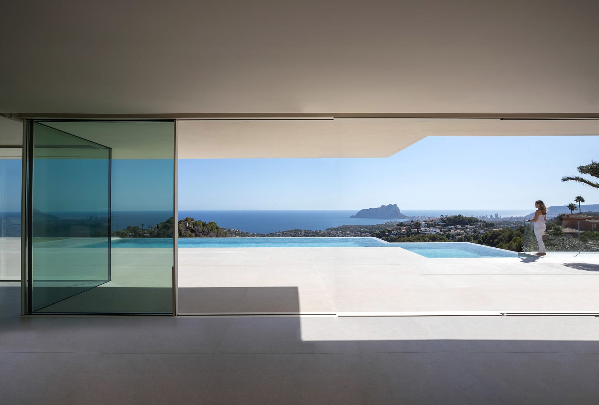 Open modern living space with white interior, large windows, and ocean views through glass doors
