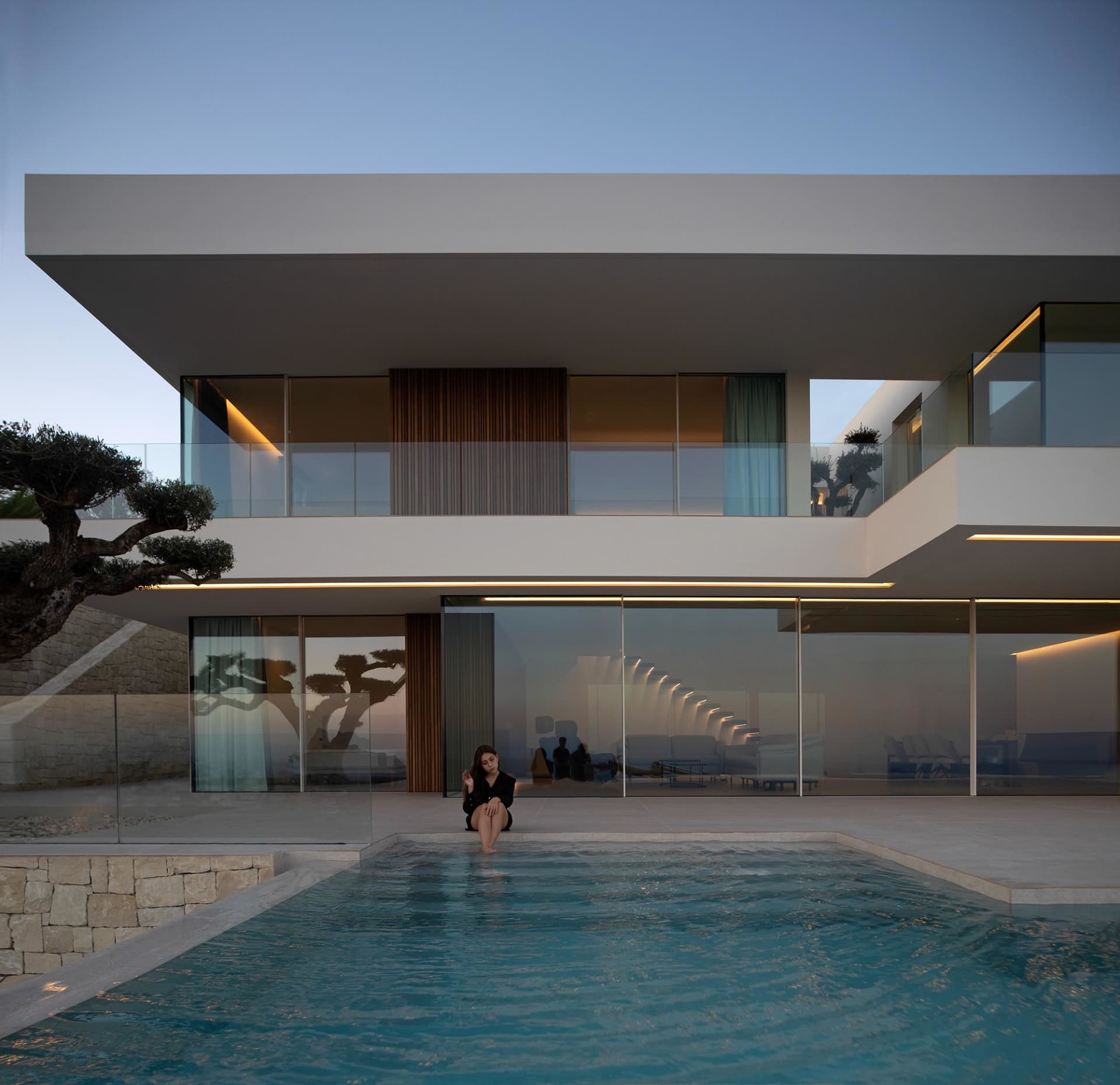 A modern pool scene with clear water, surrounded by a large white building and people relaxing in the area