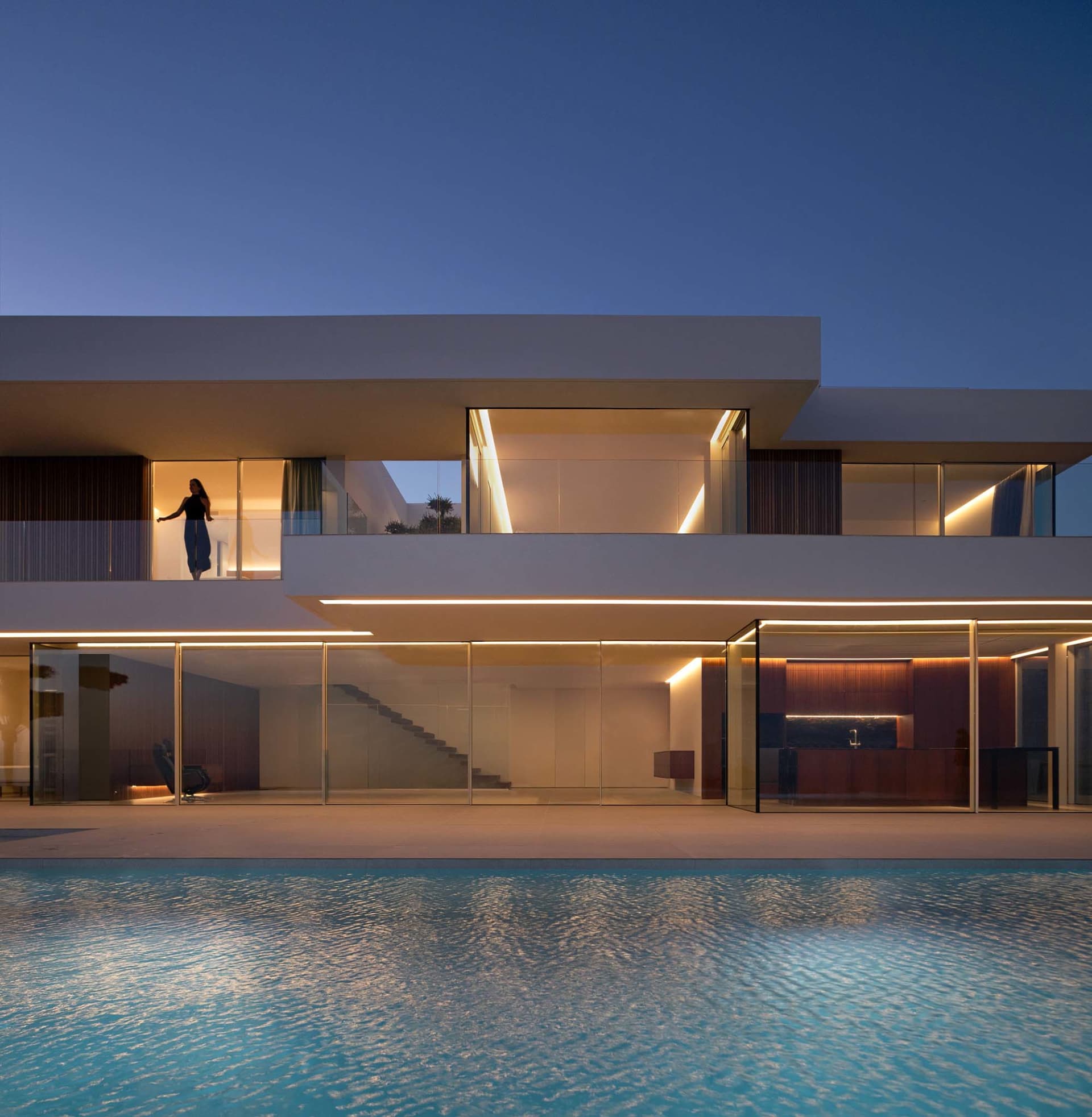 A modern white house with glass walls, a swimming pool, and a spacious living area with a couch and dining table