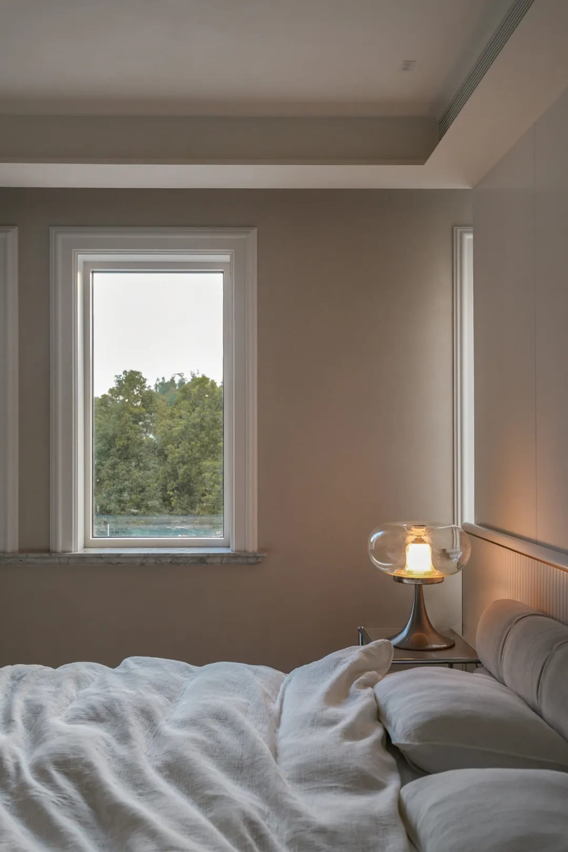 A bedroom with a large window, a neatly made bed, and two nightstands, creating a calm and inviting atmosphere