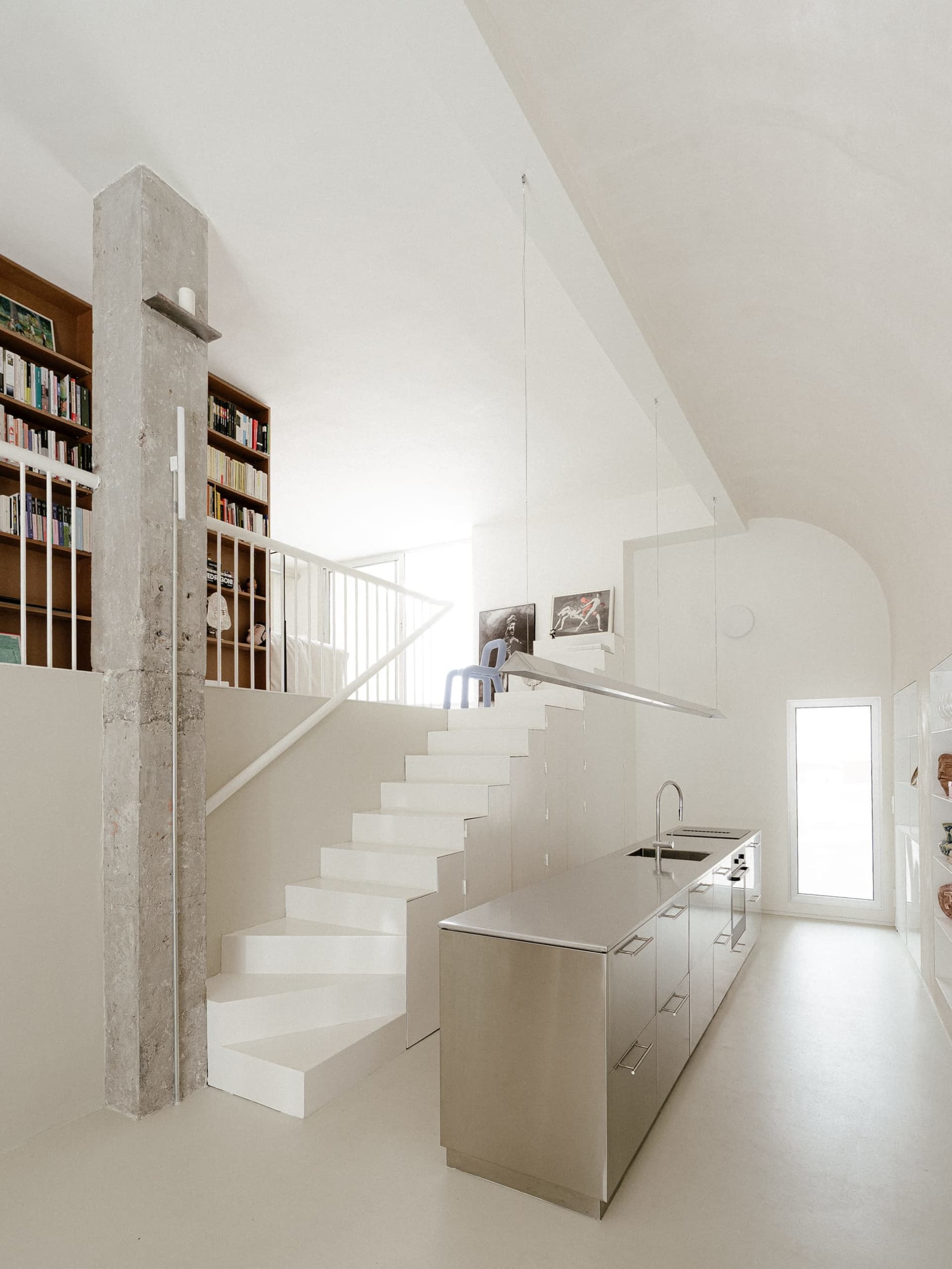 Modern kitchen and living area with stainless steel appliances, a couch, bookshelf, and dining table