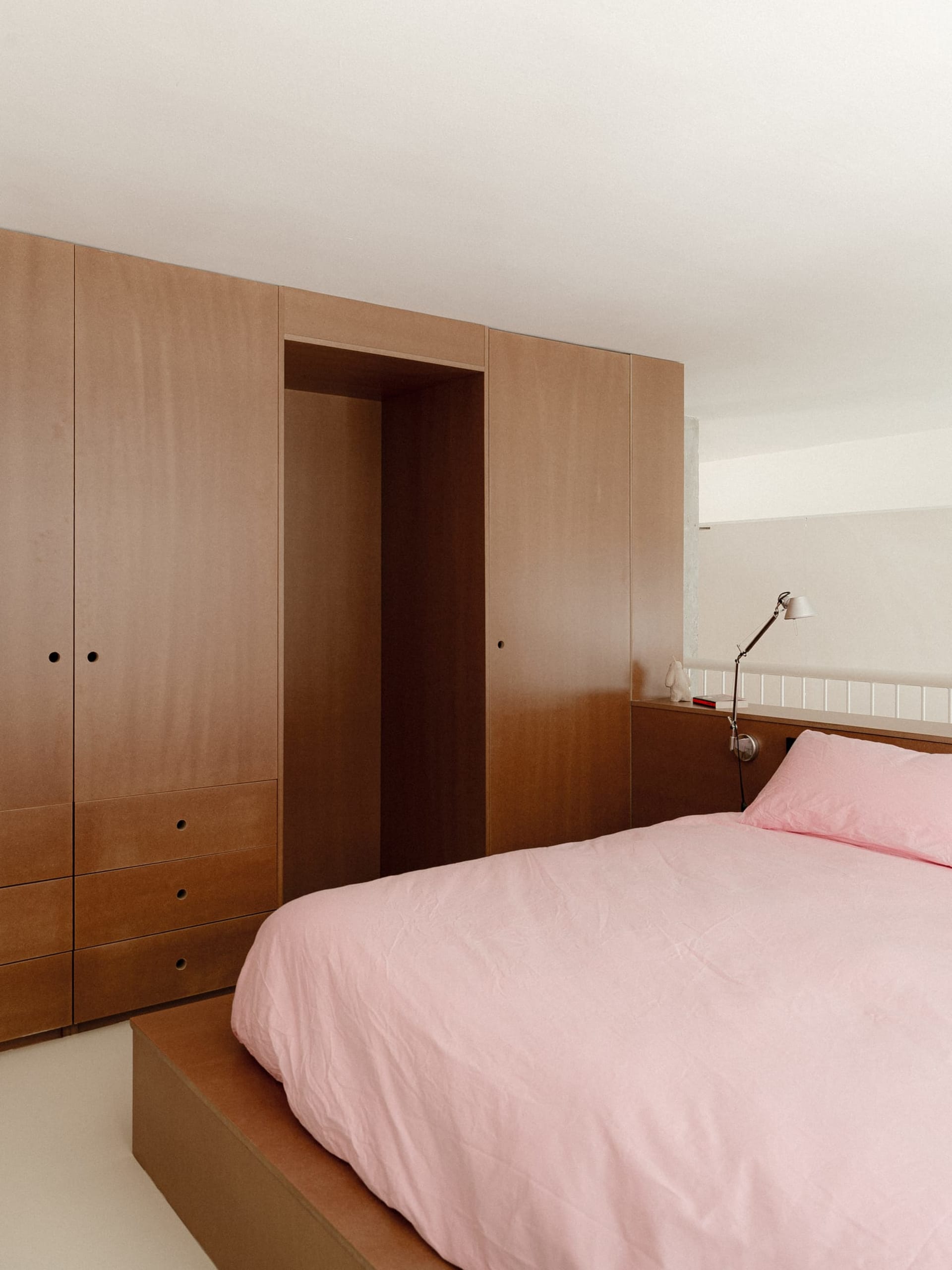 A cozy bedroom with a large bed, pink blanket, nightstands, and a dresser, creating a warm and relaxing atmosphere
