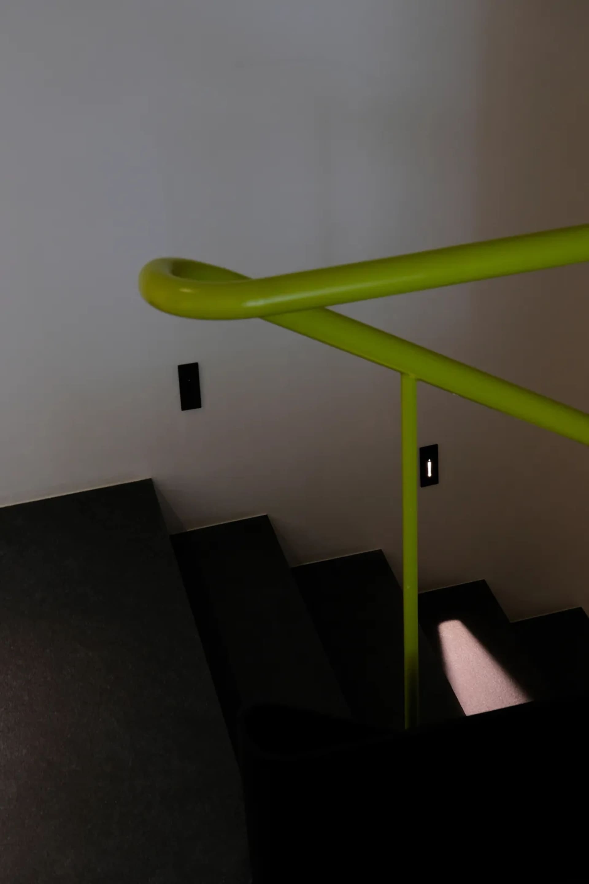 A photo of a staircase with a yellow handrail, set in a modern building with a residential or commercial atmosphere, featuring concrete or similar construction materials
