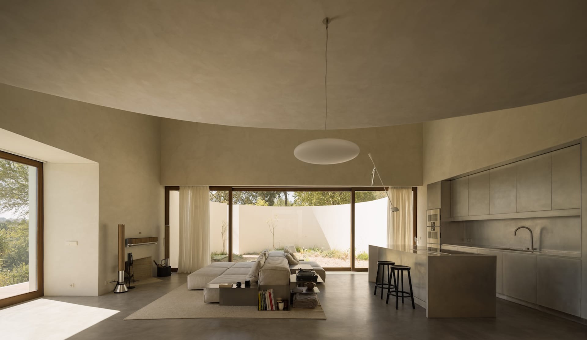 Modern living room with a circular window, two couches, a chair, and a dining table, with books scattered throughout