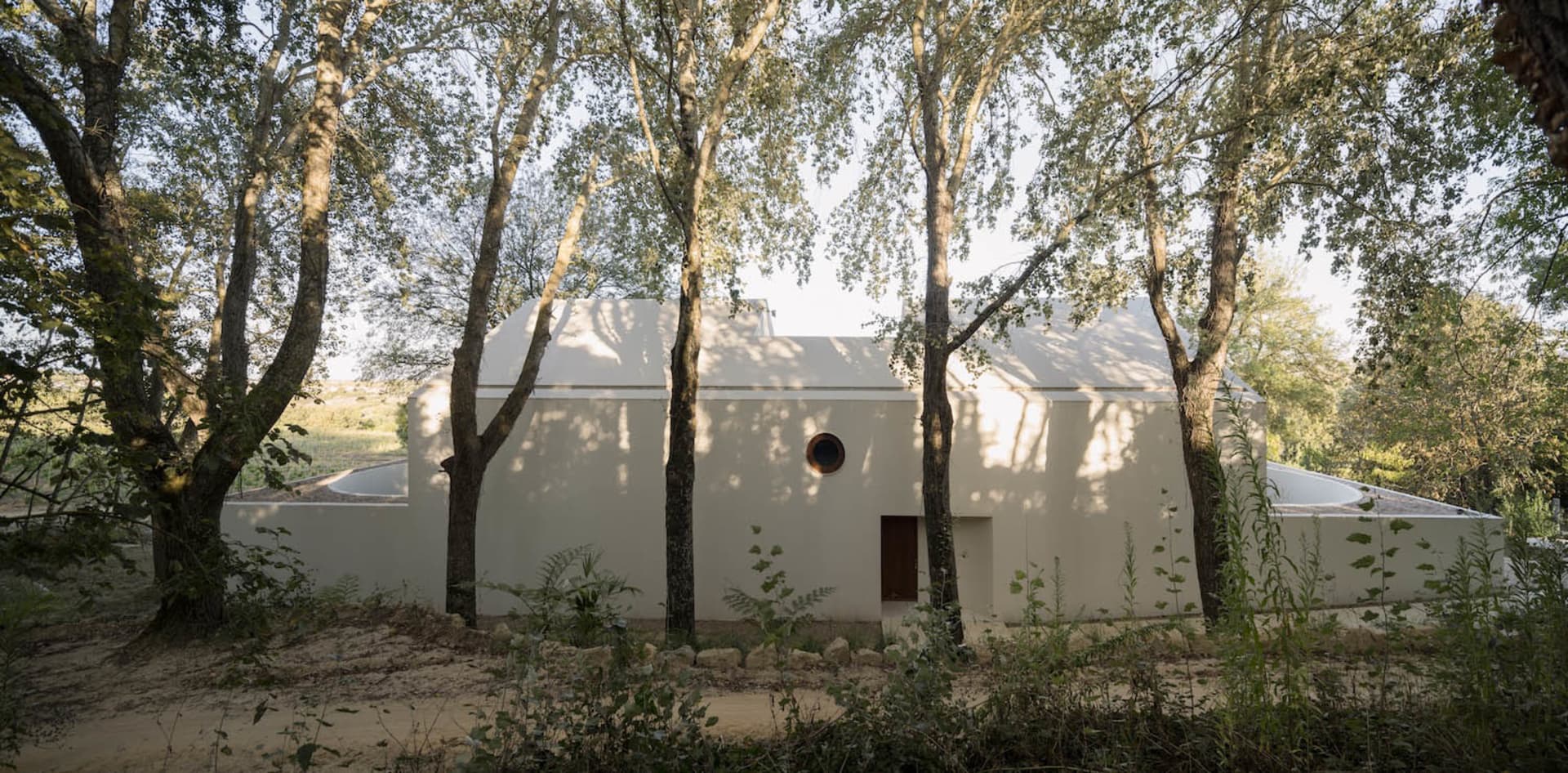一座白色建築物的渲染圖，配有圓形窗戶，周圍環繞樹木，位於郊區或半鄉村地區