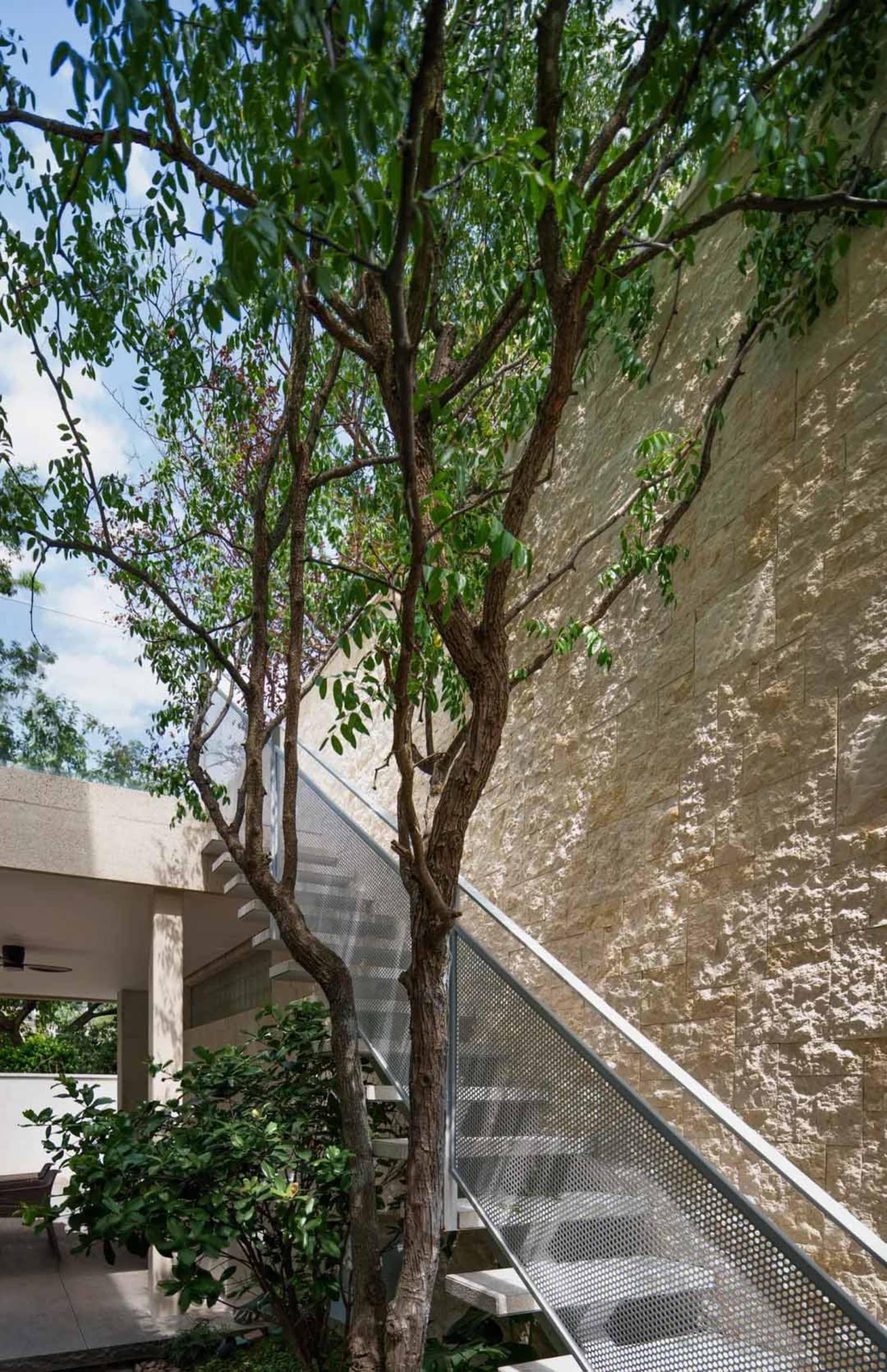 A modern staircase with metal steps and a brick wall in the background, with a tree in front and a second-story balcony above