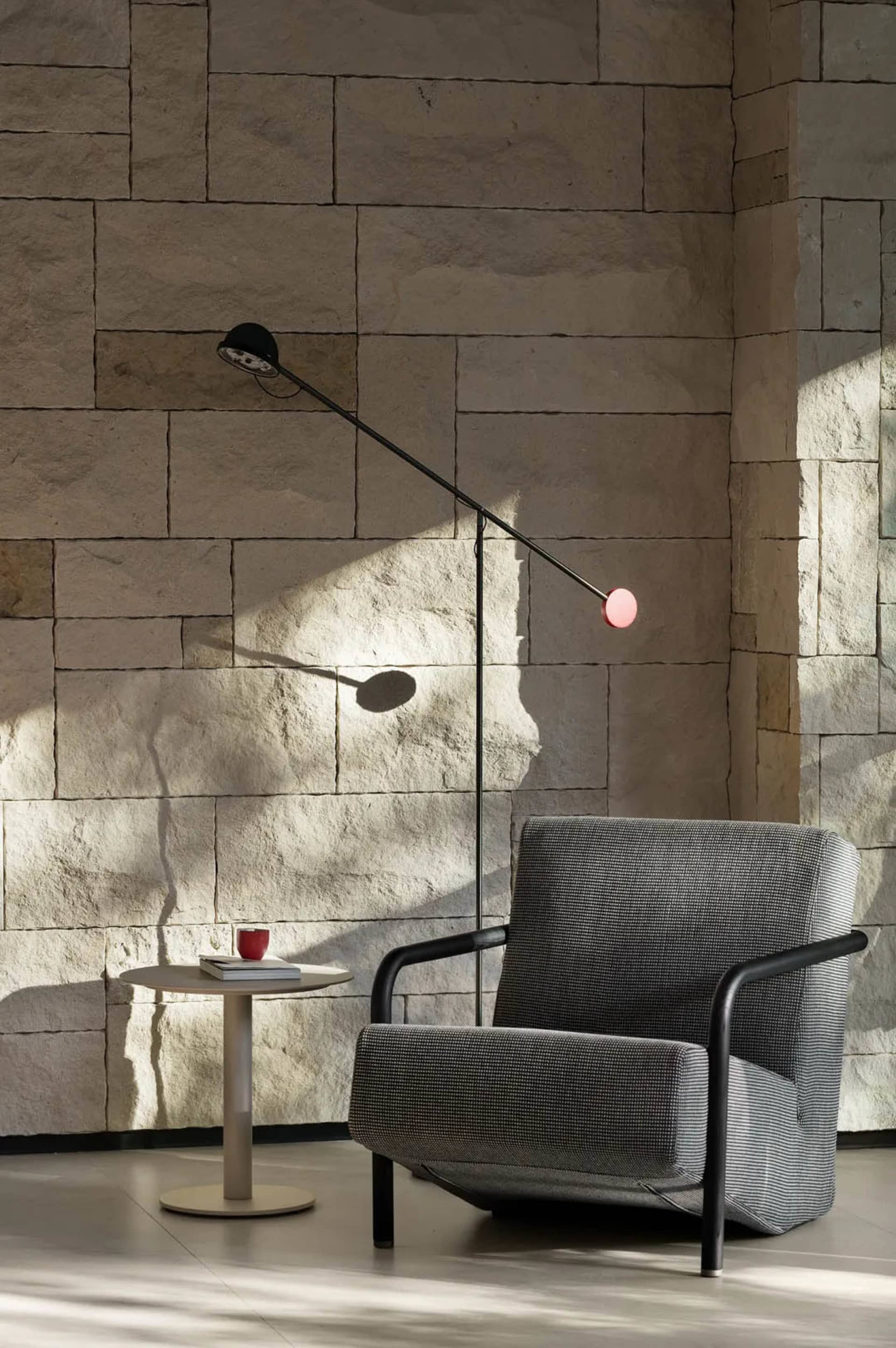 A gray chair sits in front of a stone wall, accompanied by a dining table and two cups on nearby surfaces, creating a calm and inviting atmosphere