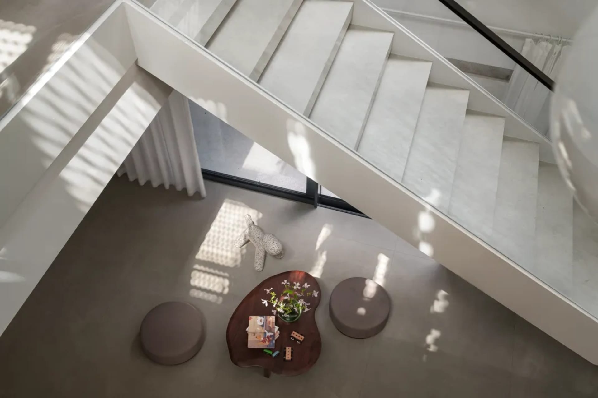 Bright open living area with a white staircase, two couches, a dining table, and a potted plant, surrounded by ample seating options