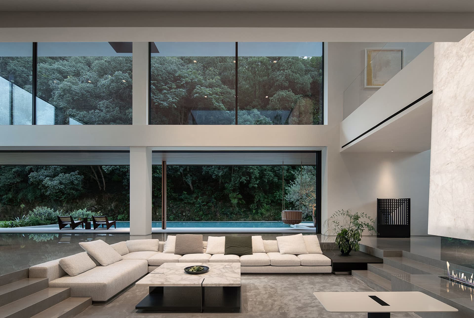 Open modern living area with a white couch, glass wall, chairs, and dining table, giving off a clean and minimalist vibe