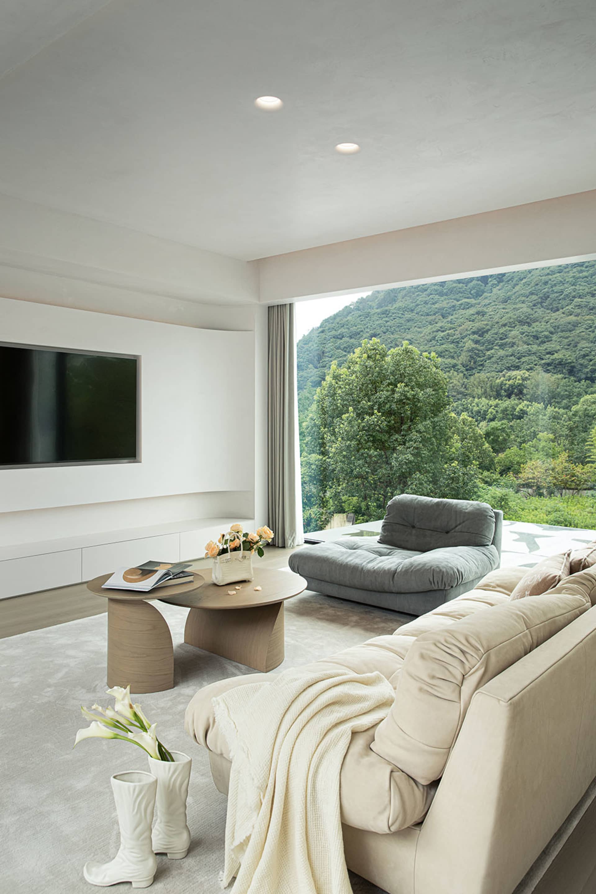 Cozy living room with a modern design, white walls, wooden floors, a large couch, a chair, and a flat screen TV, with vases placed throughout the space