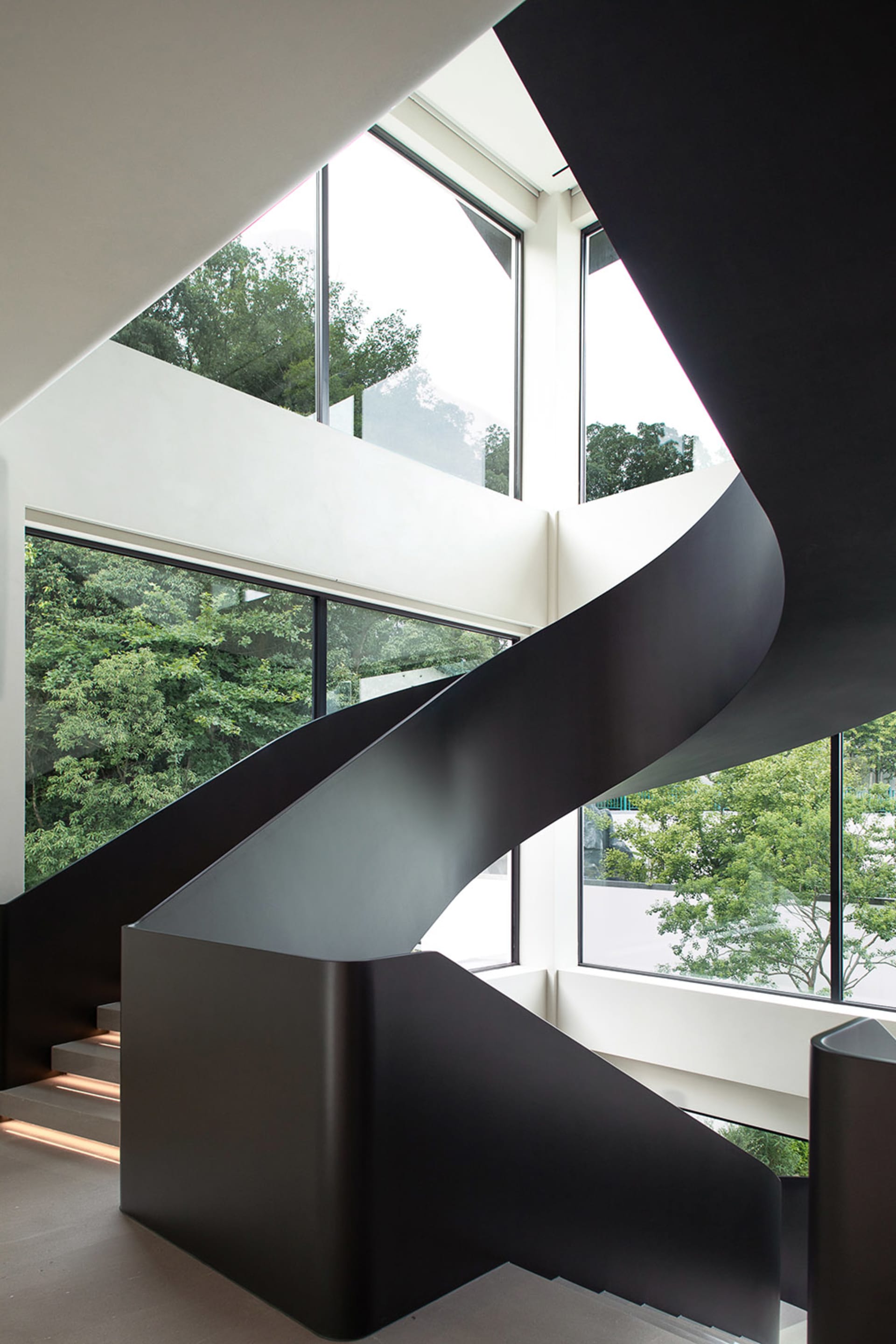 A modern staircase with black railings and metal steps, set against white walls and natural light from multiple windows
