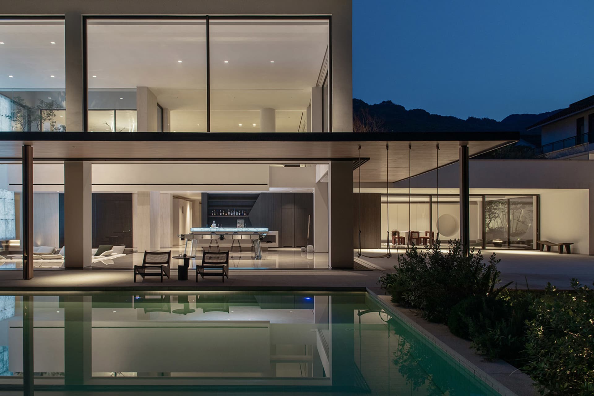 A modern indoor swimming pool area with a glass enclosure, surrounded by chairs and dining tables, creating a relaxing and inviting atmosphere
