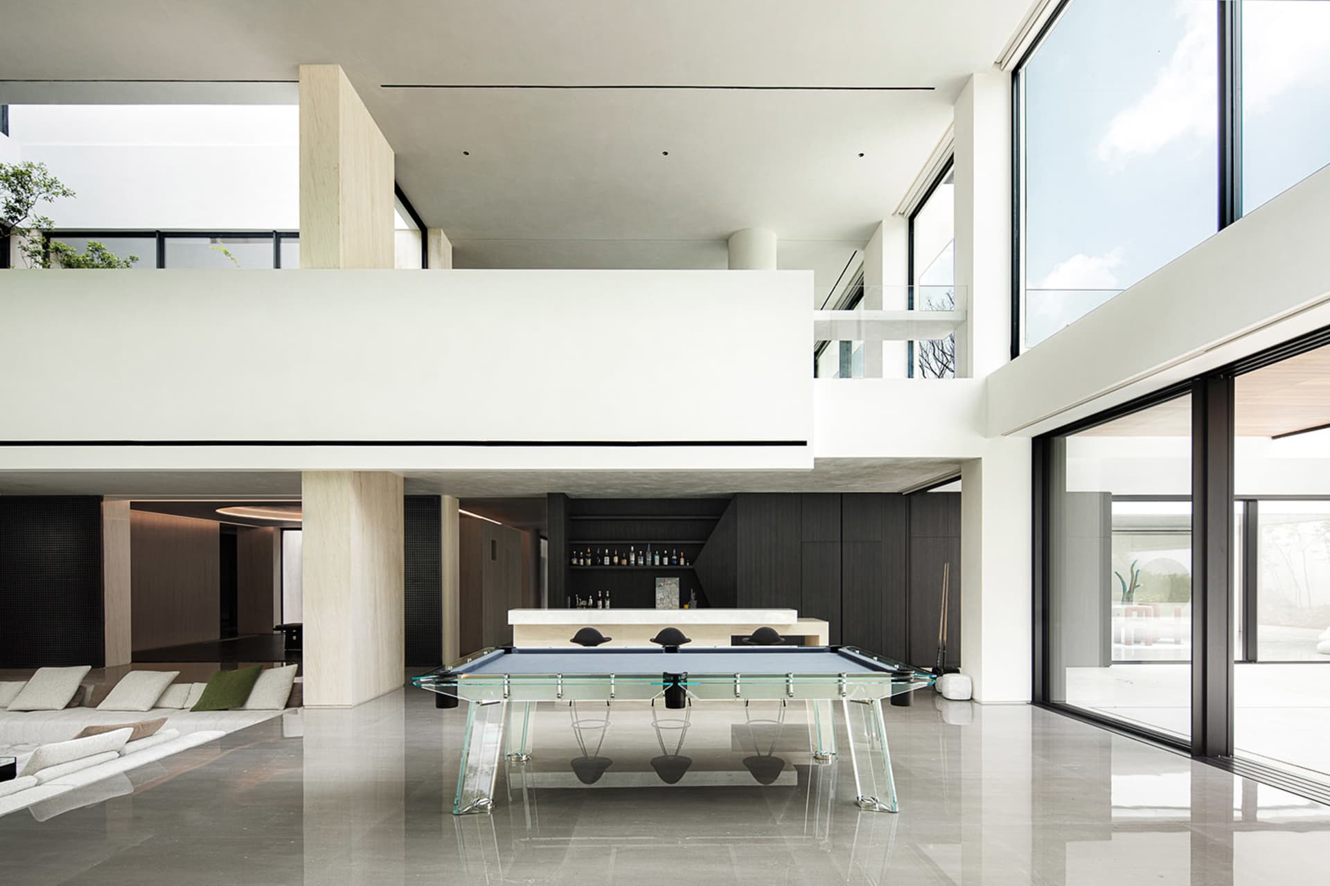 Spacious open concept living area with a glass dining table, chairs, a bar area, pool table, and decorative bottles, set in a modern home with a contemporary and stylish interior design