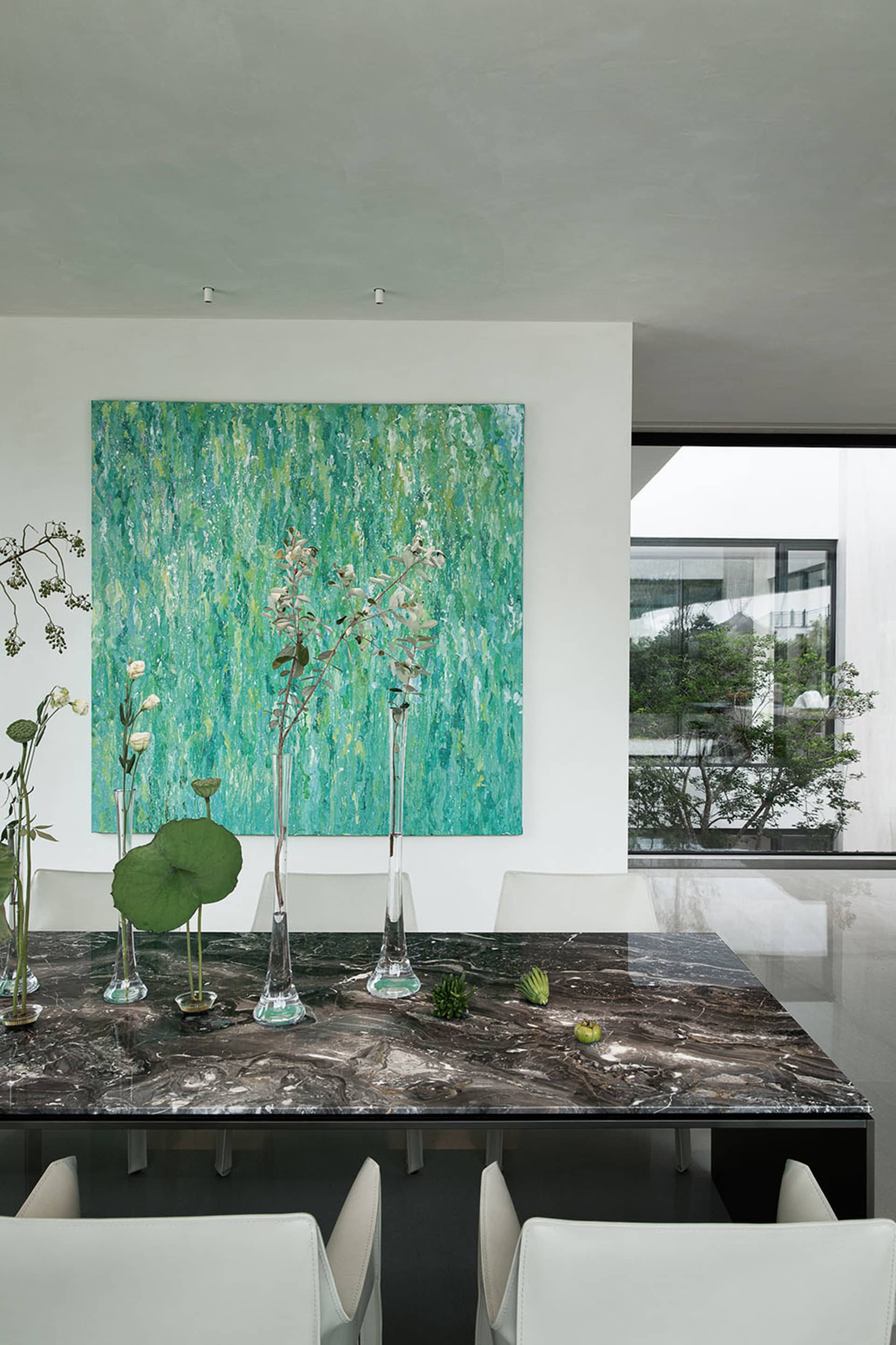 A cozy dining space with a table, chairs, vases with flowers, potted plants, and a painting on the wall