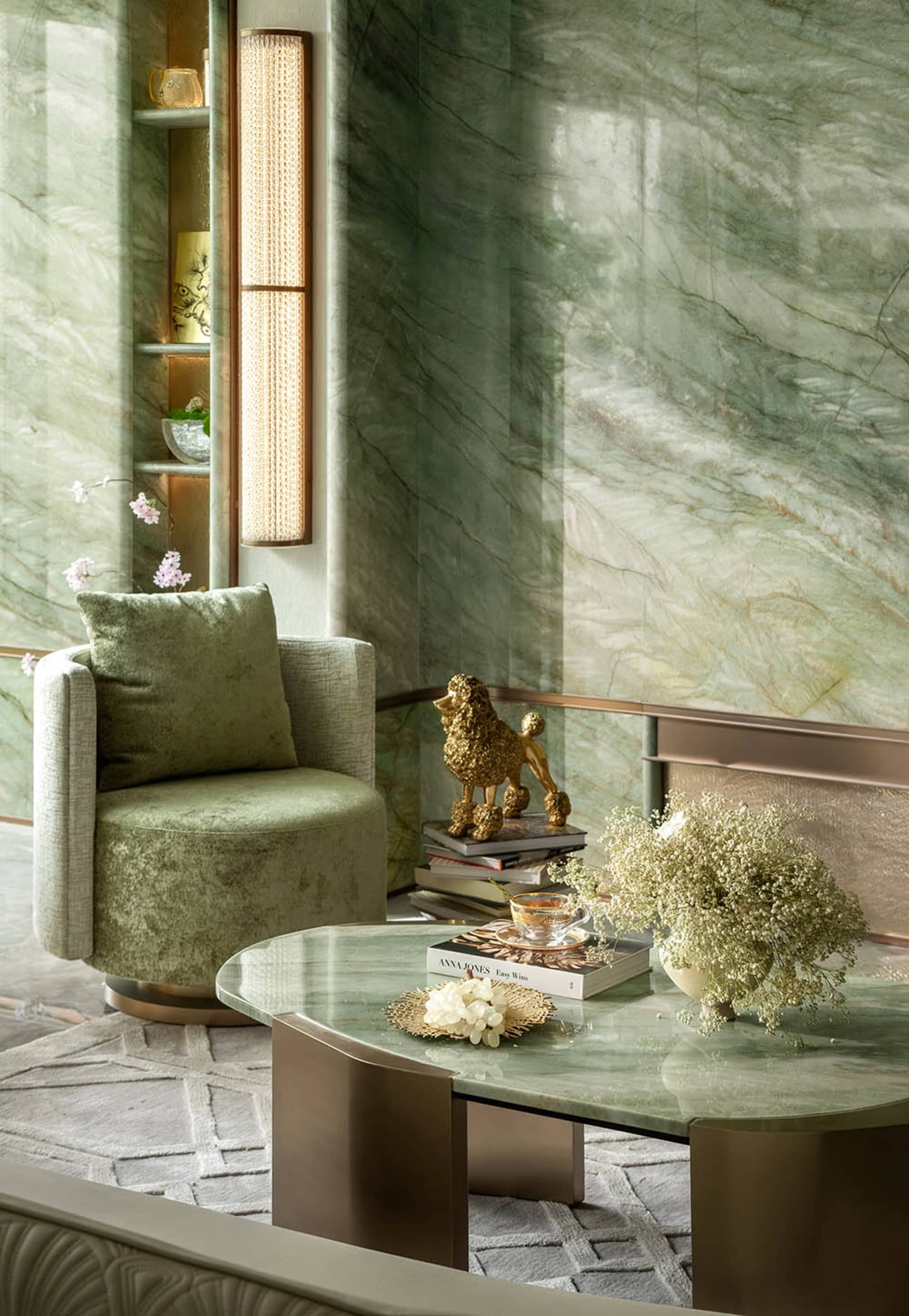 A modern living area with a green chair in front of a glass table, surrounded by books, vases, and a bowl, creating a cozy atmosphere