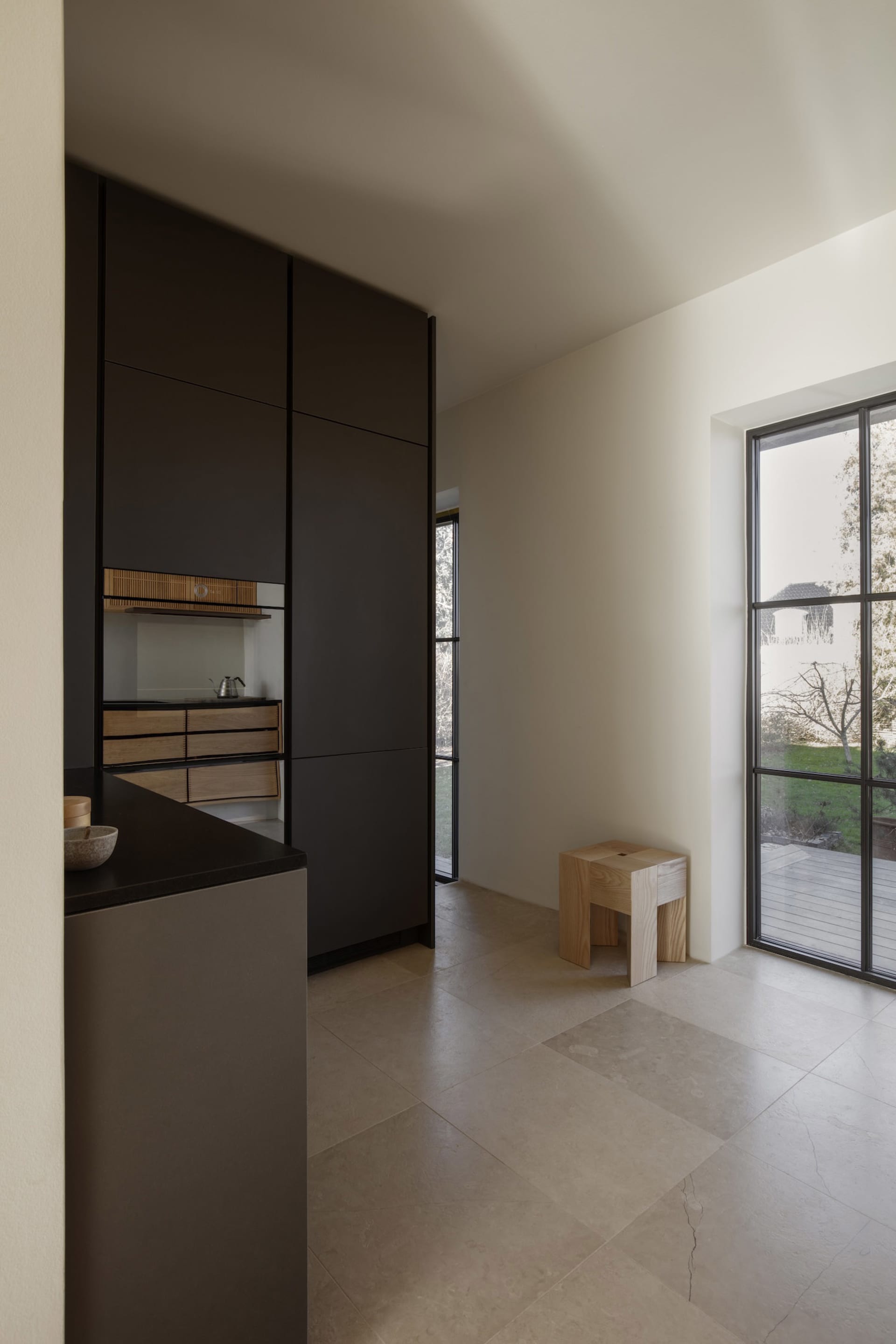 Empty kitchen with black cabinets, white walls, and two windows, well-lit and minimalist