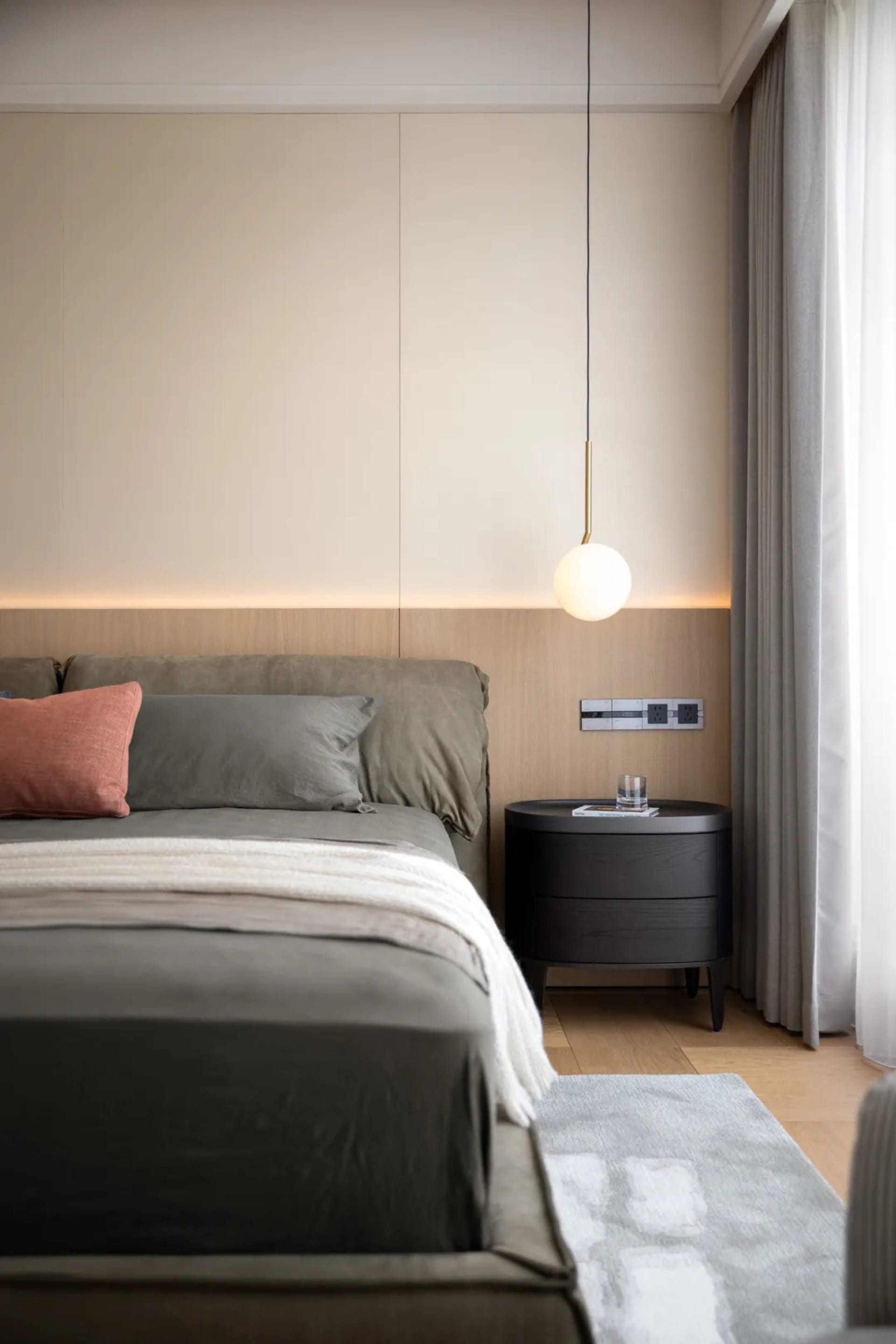 Cozy bedroom with a large bed, grey comforter, and wooden floor, set against a minimalist white backdrop