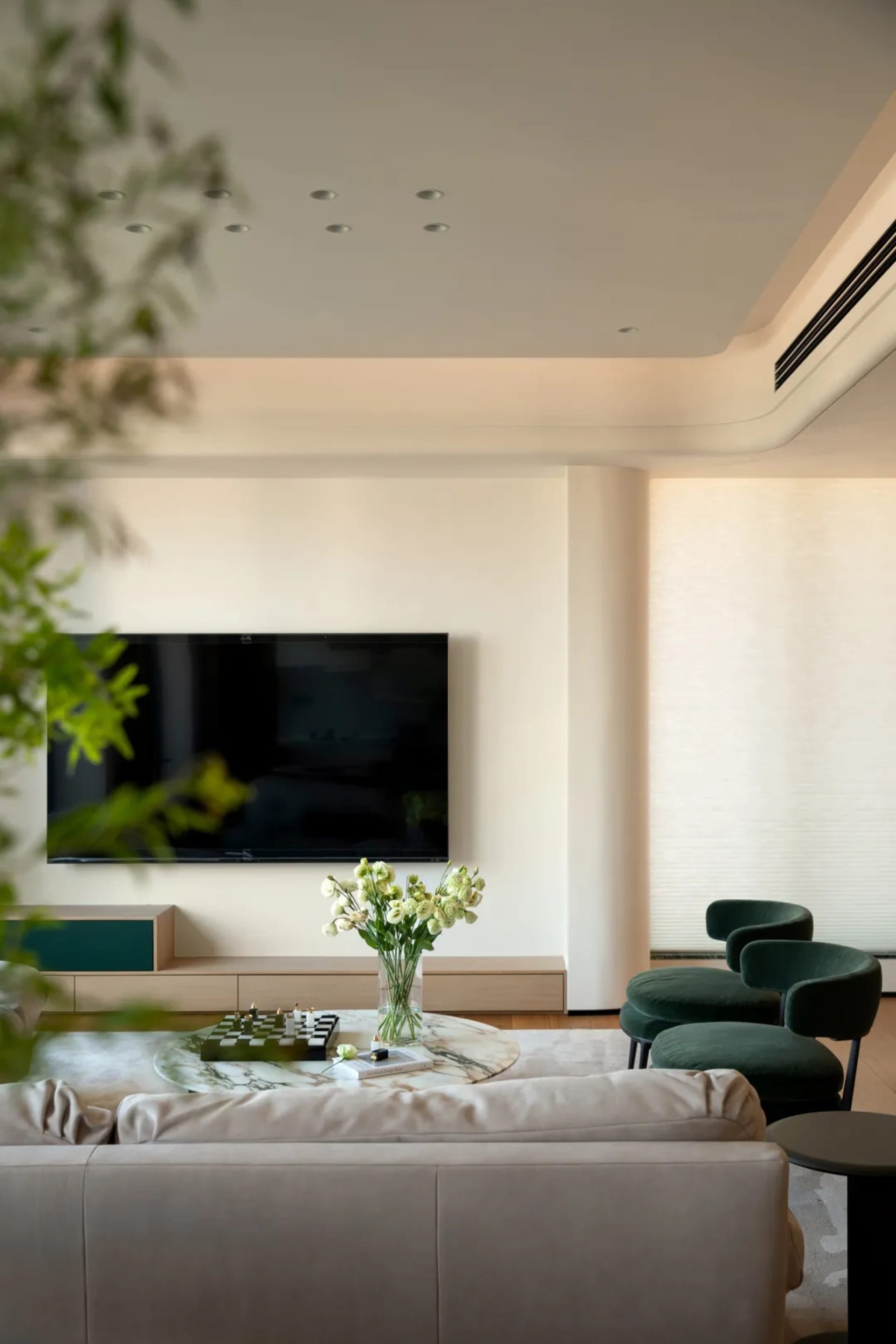 A modern living room with two couches, three chairs, and a large flat screen TV, featuring white walls and wooden furniture