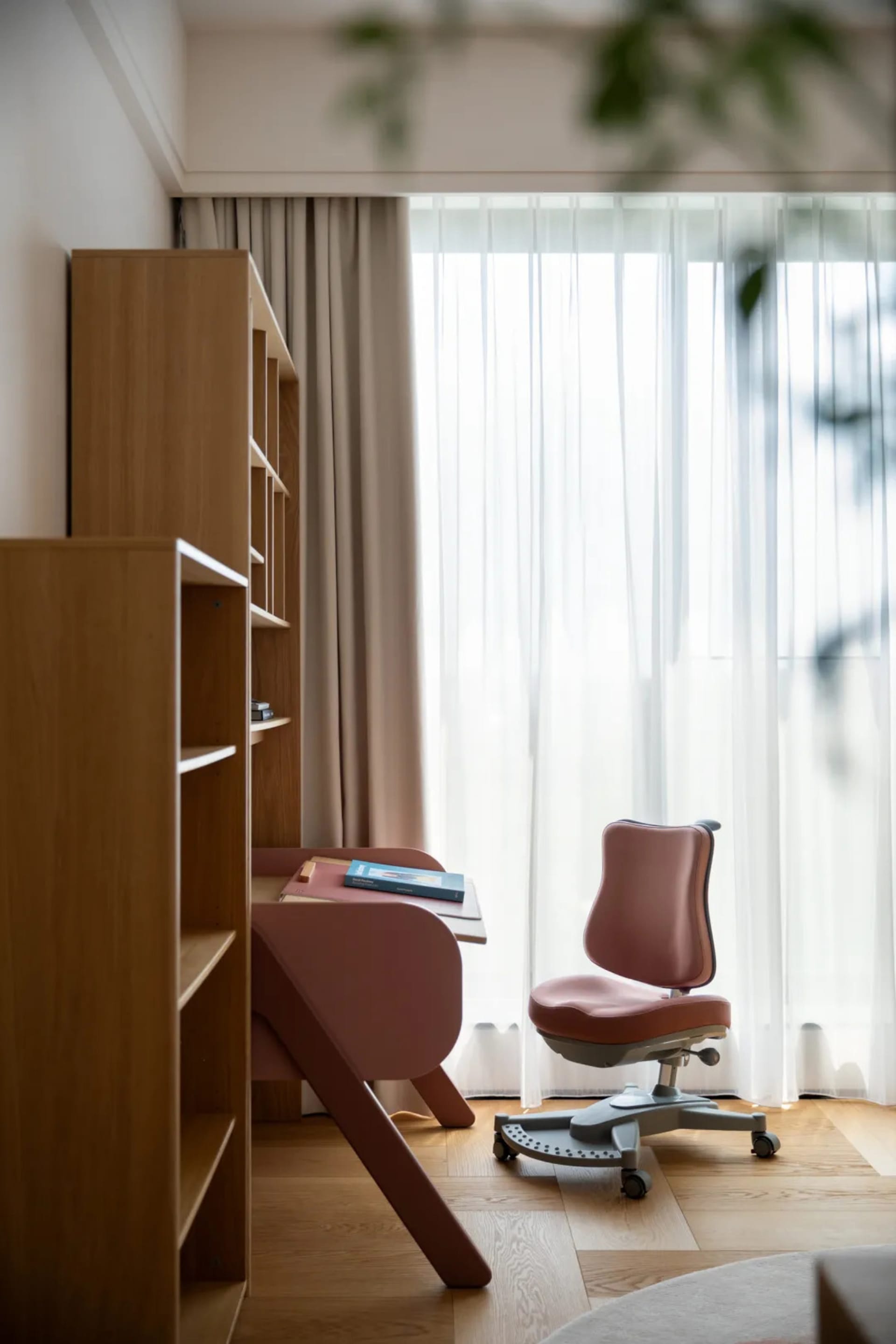 A calm and organized office space with a wooden desk, two chairs, a book, and natural light from a window