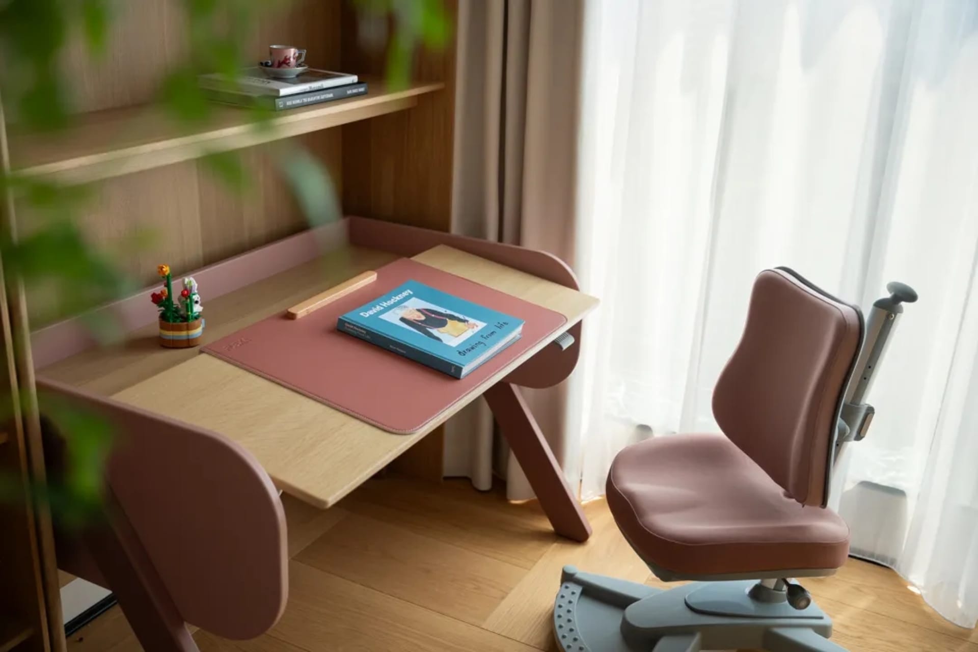 A calm and organized office space with a pink desk, two chairs, and a book, set against a neutral-toned background