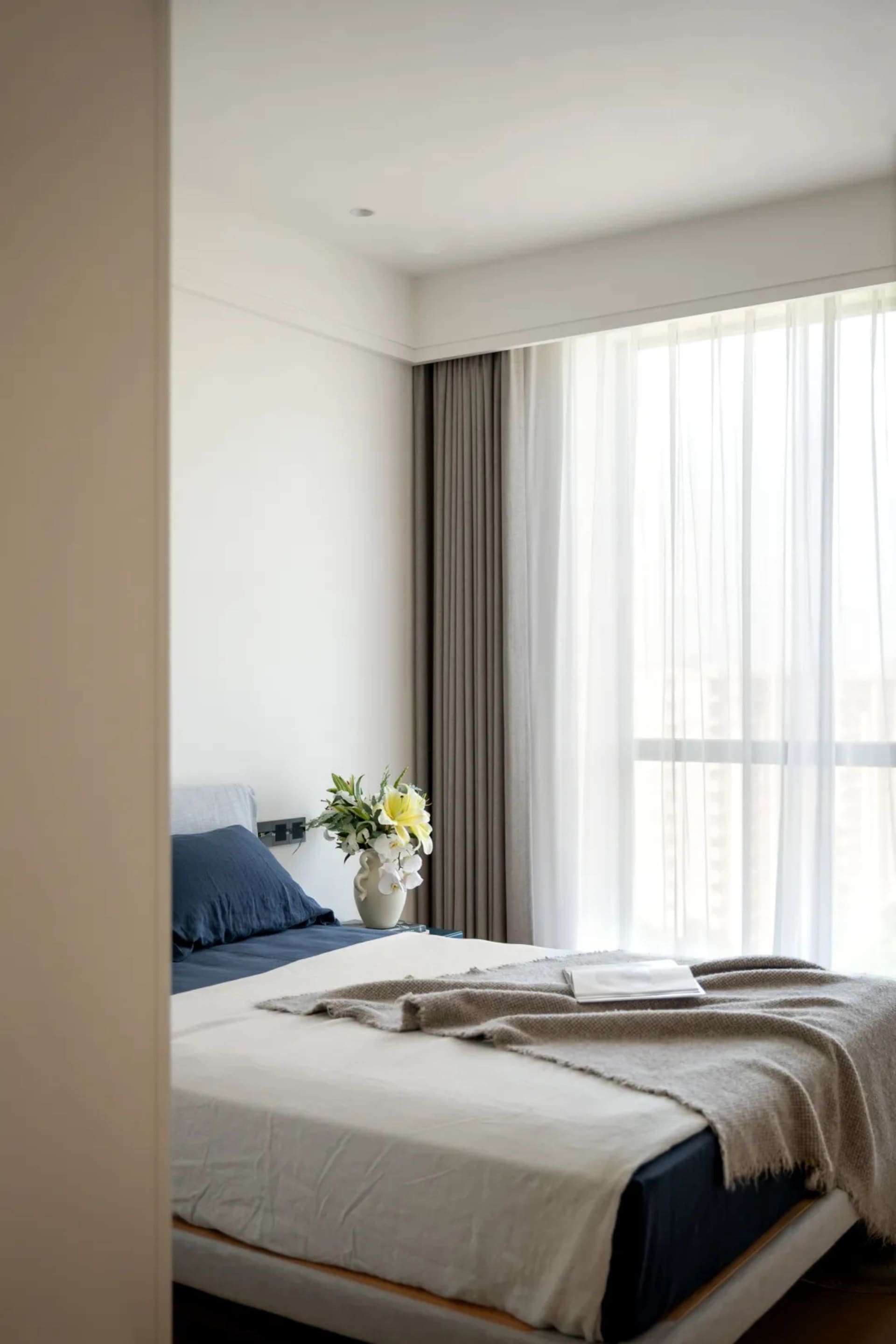 A serene bedroom with a white bed, two vases, and a book, surrounded by natural light from a window