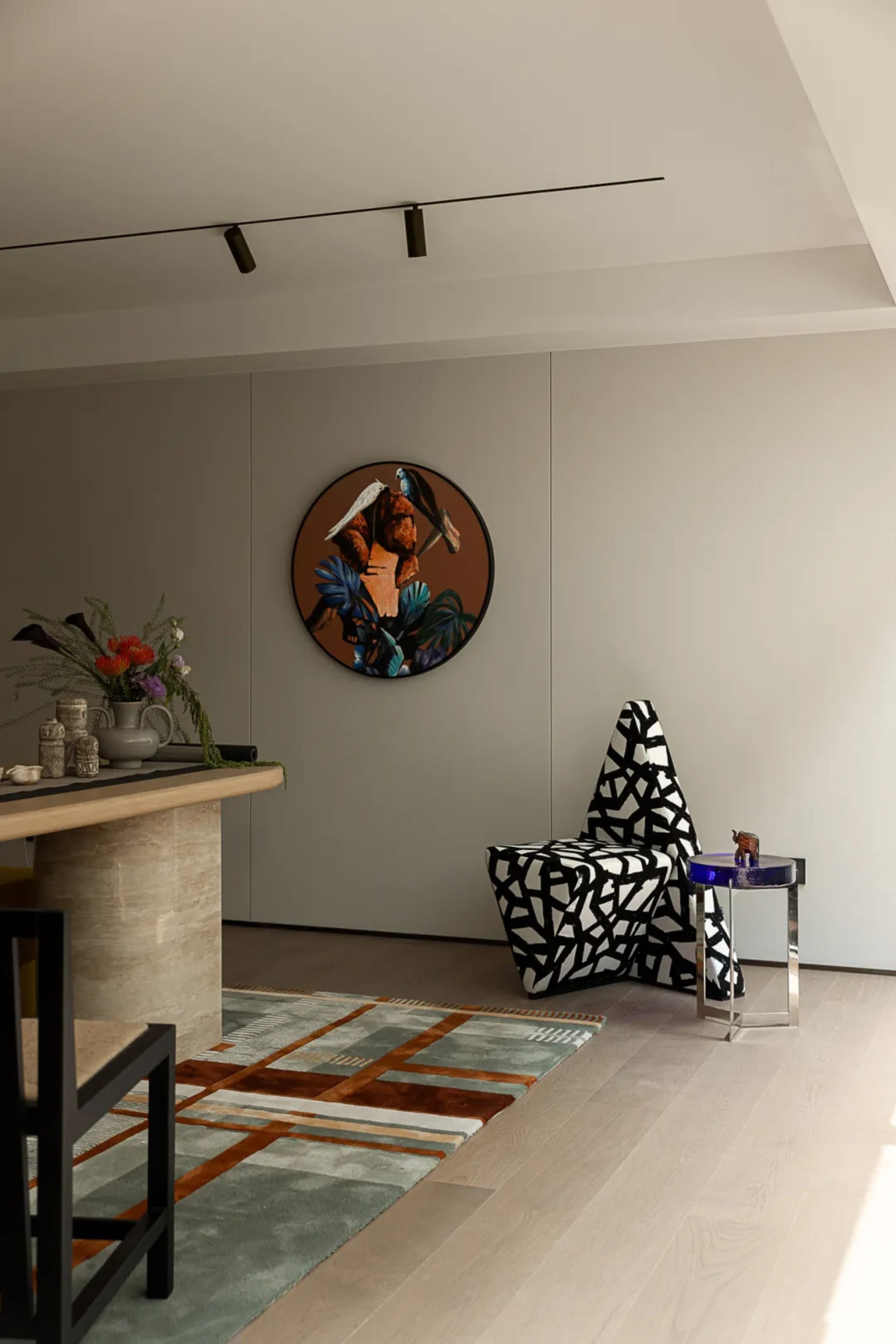 Cozy modern living space with a chair, dining table, couch, and vases, featuring a large wall clock and wooden furniture