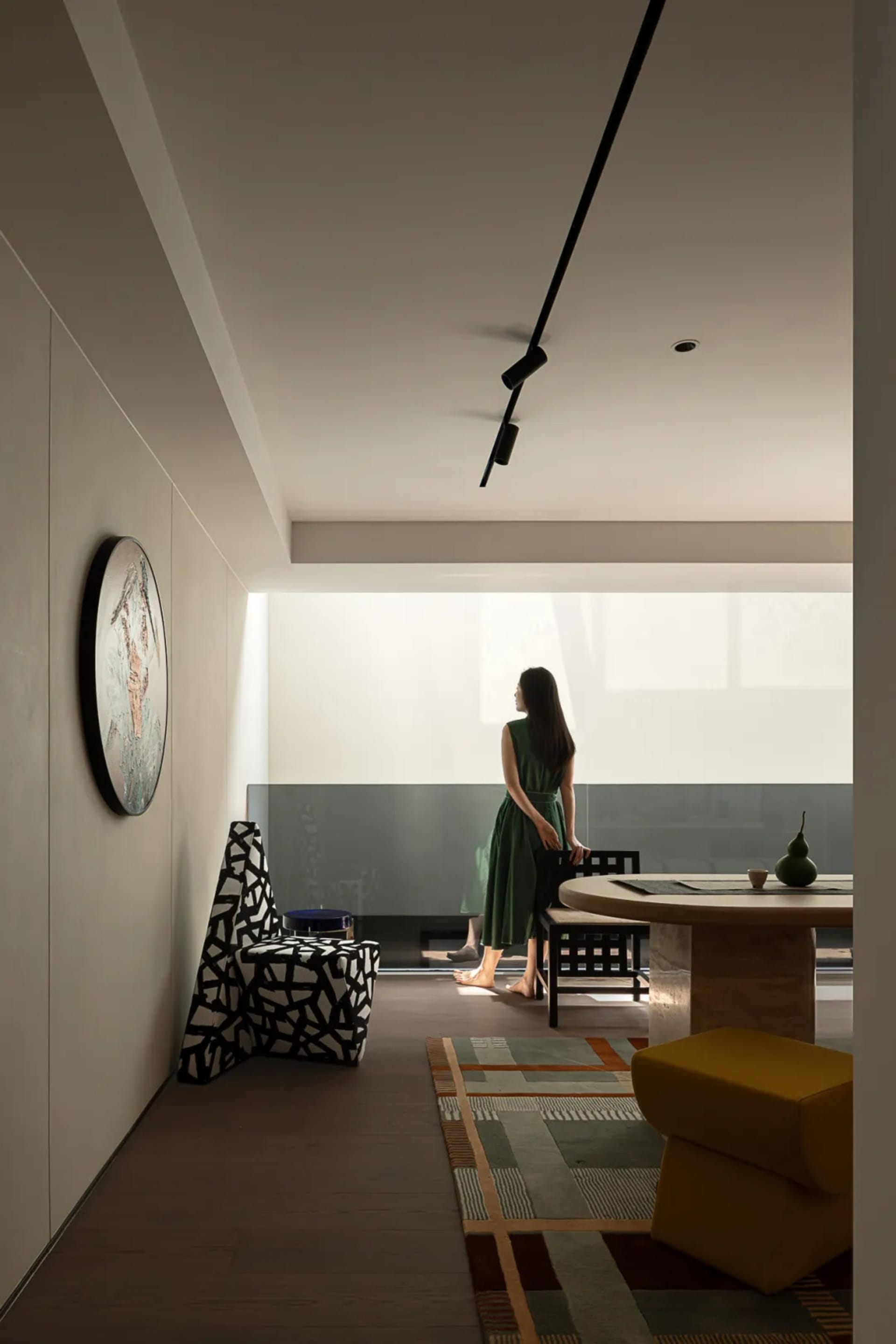 Modern dining space with a black and white theme, featuring a dining table and chairs, a clock on the wall, and a woman standing near the table