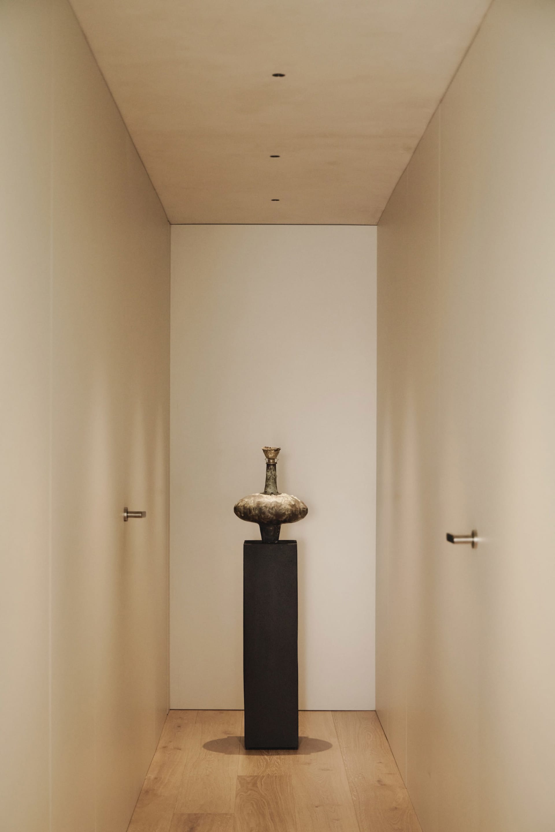 Empty hallway with white walls, a black metal vase on a pedestal, and a minimalist aesthetic