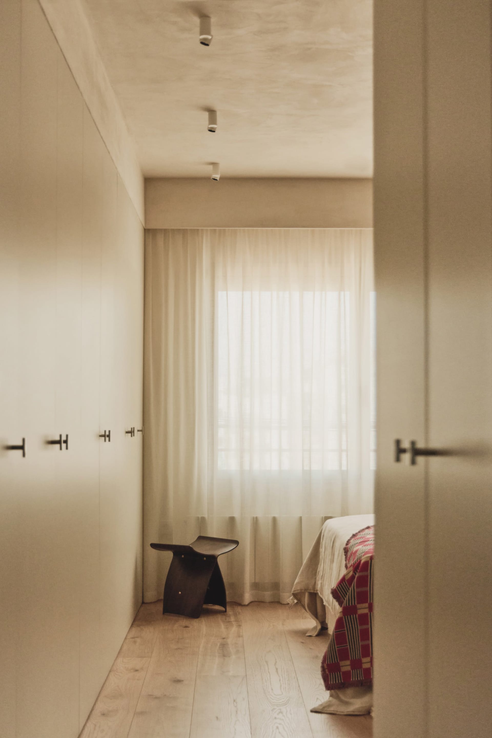 A serene bedroom with two beds, a chair, and a white wall, with a window letting in natural light