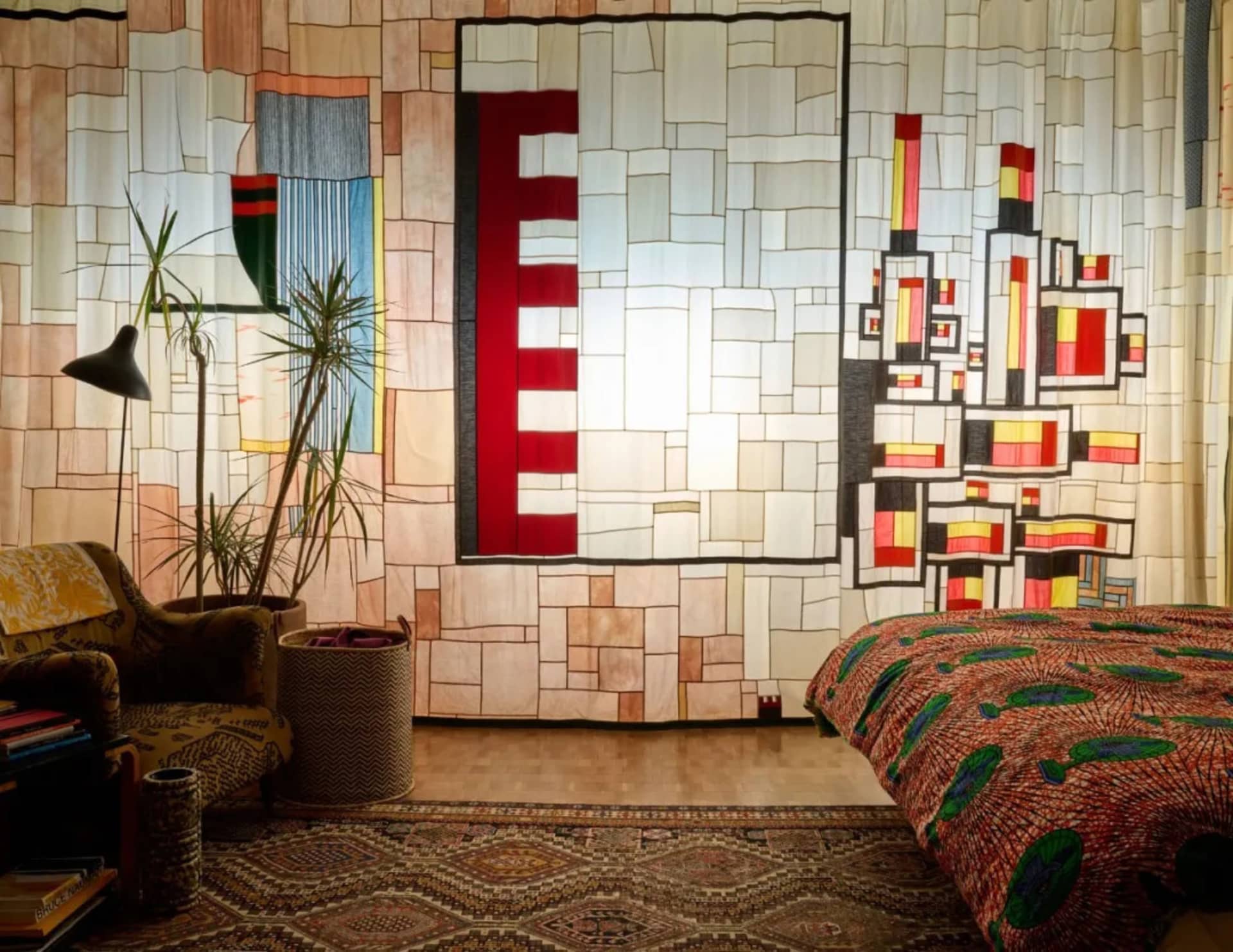 Cozy bedroom with a large bed, colorful mosaic wall, two chairs, and a potted plant, creating a warm and inviting atmosphere
