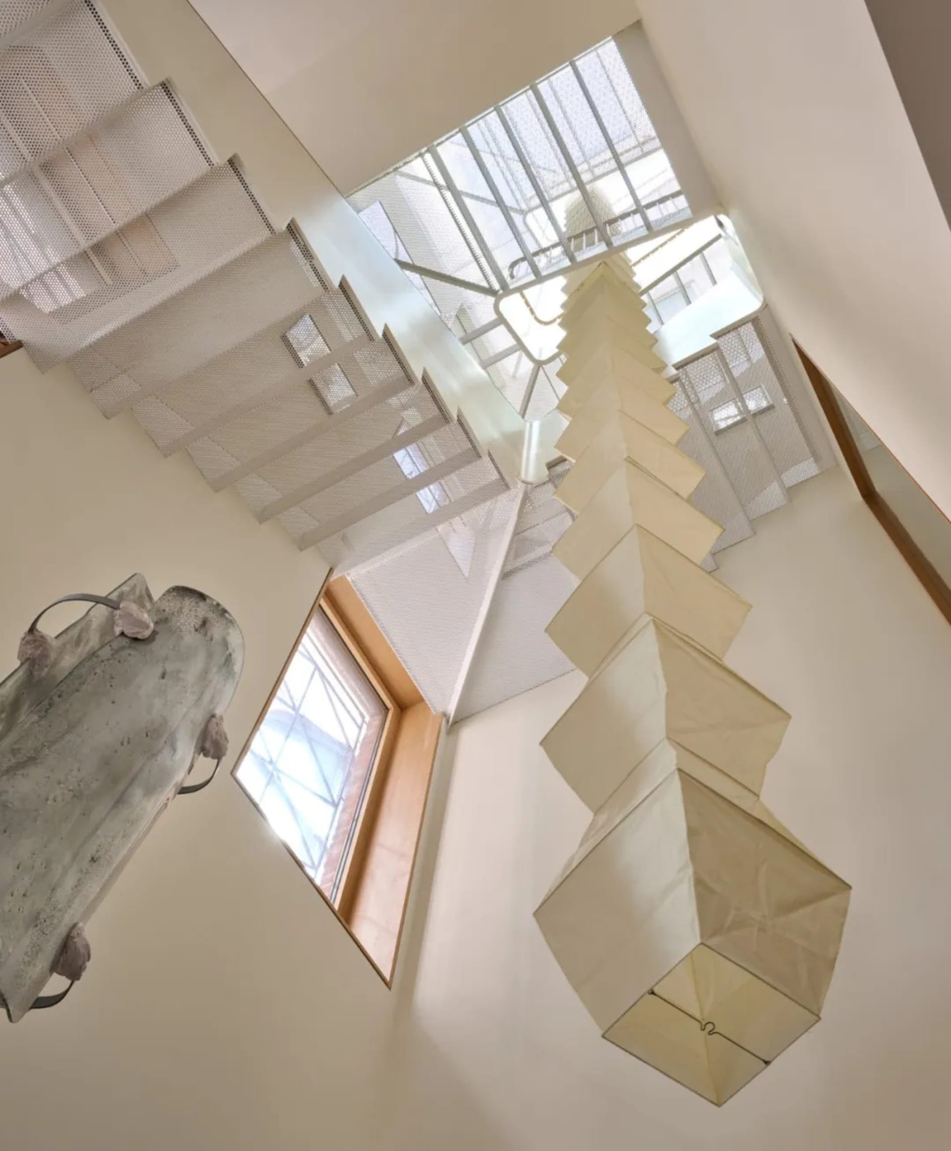Open modern stairwell with white walls, a wooden railing, and artwork on display