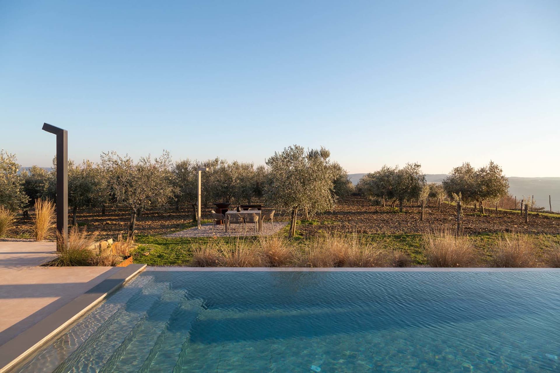 A serene outdoor pool area surrounded by trees and a patio with chairs placed around the pool for relaxation and leisure time