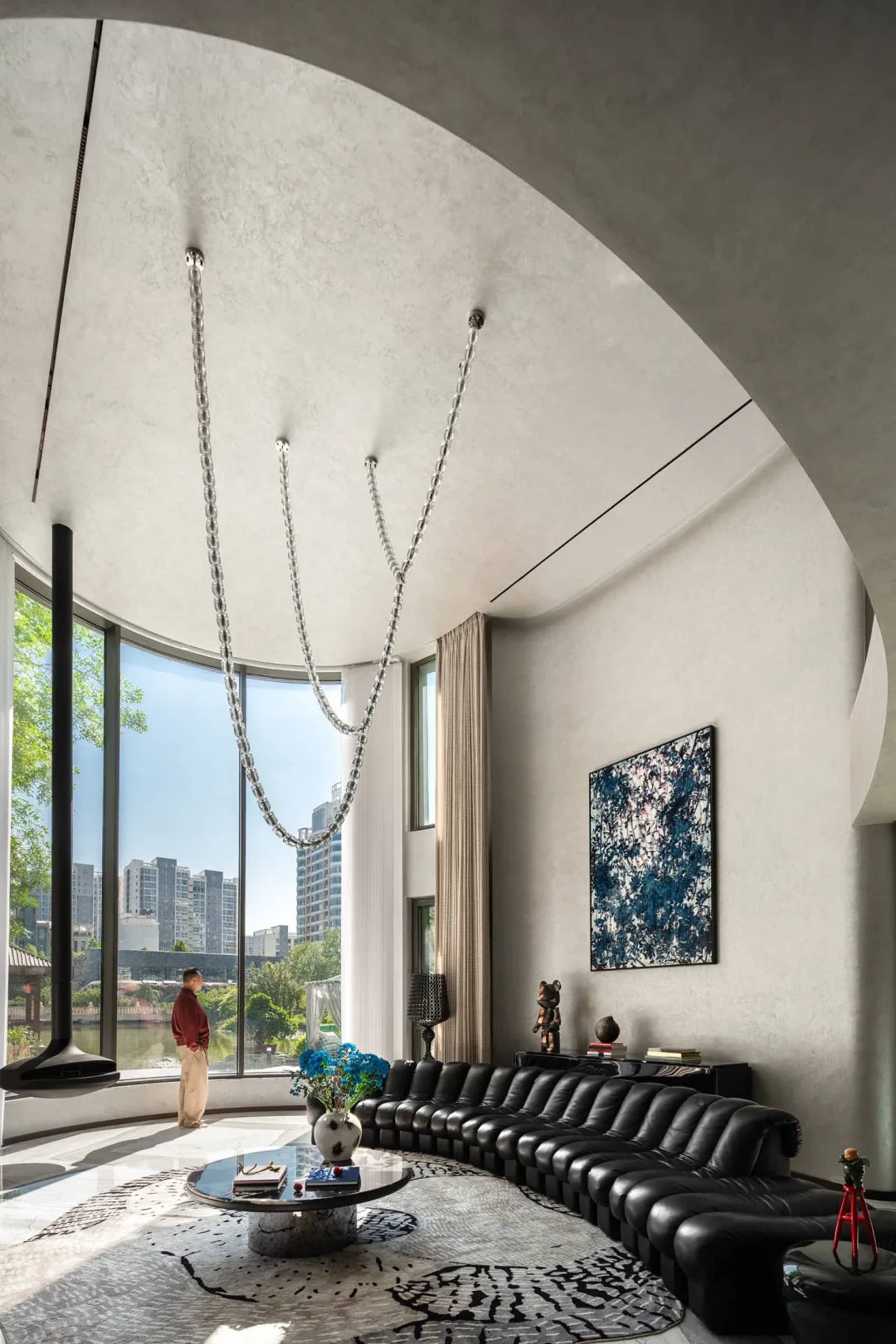 Modern living room with a black leather sofa near a window, city view, potted plants, and decorative vases